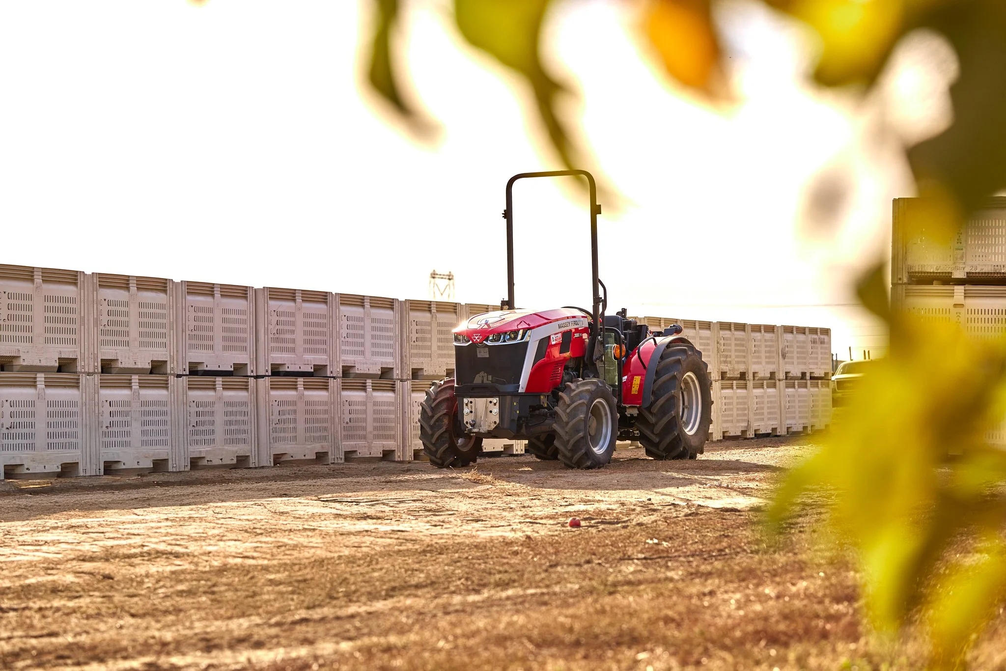 A red tractor parked on a dirt ground near a white plastic crate wall during sunset.
