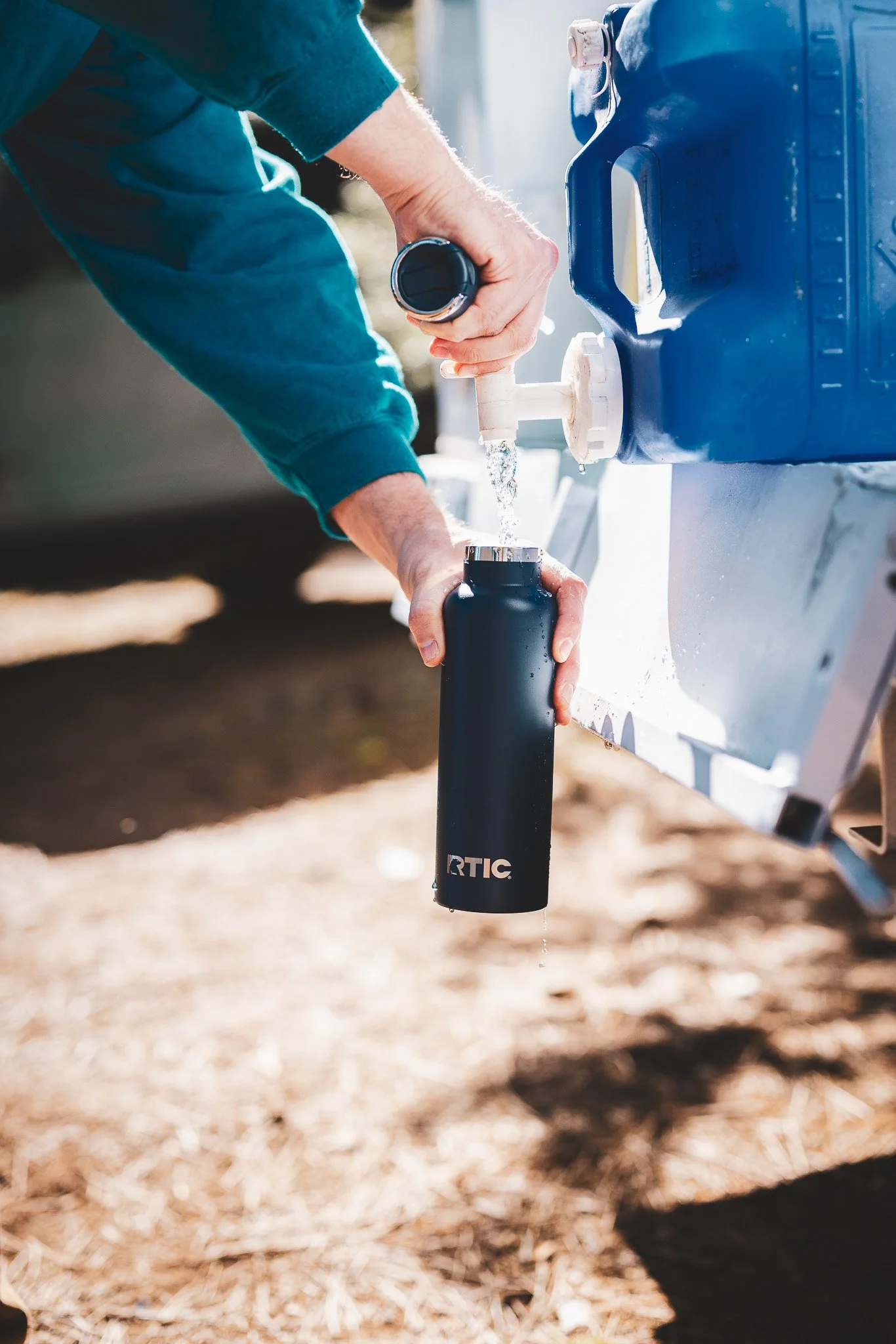 Person filling a black water bottle from an outdoor water dispenser.