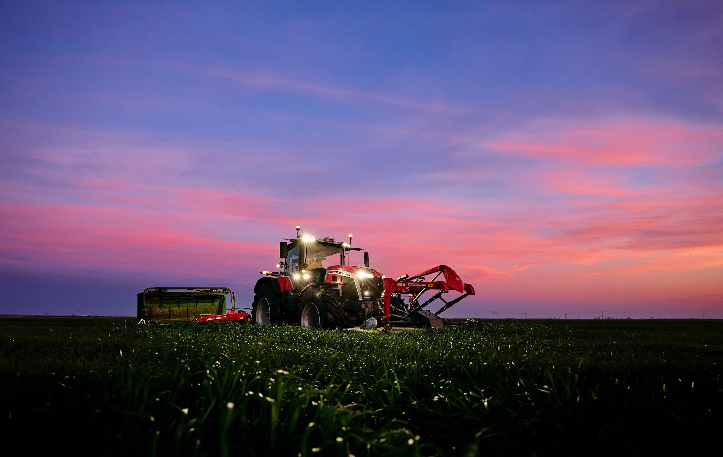 A tractor working in a field at sunset with a colorful sky in the background.