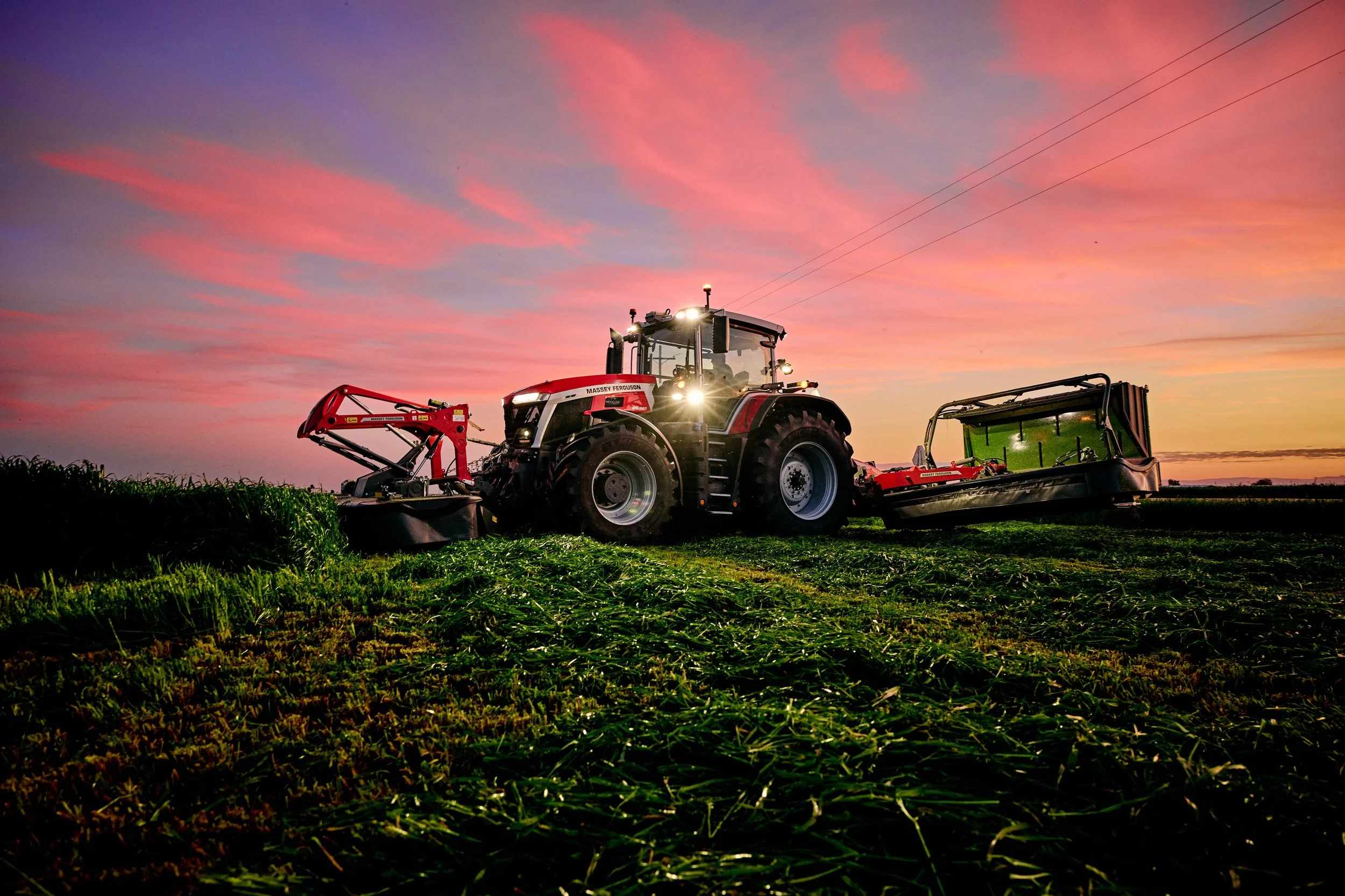 A red tractor working in a field during sunset with a colorful sky.