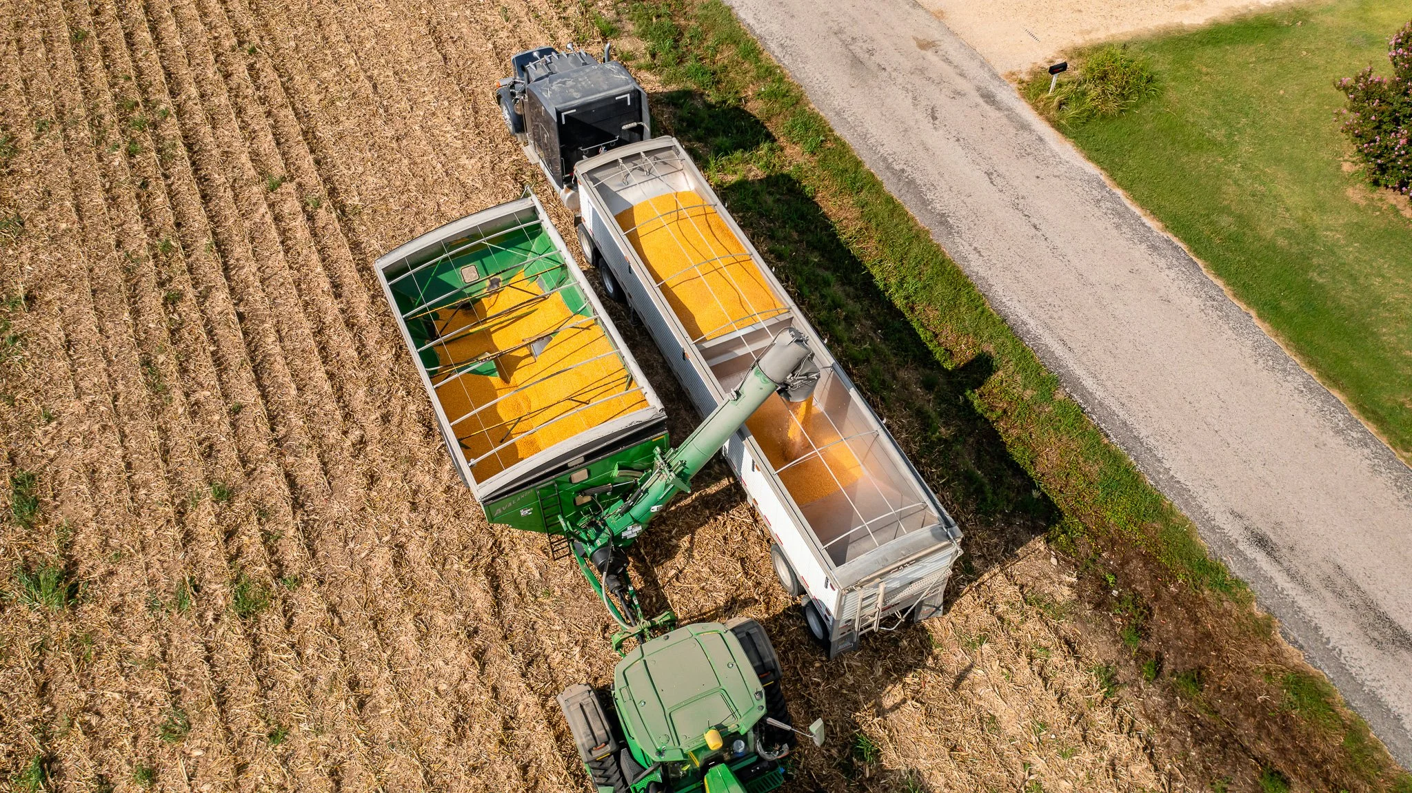 An aerial view of a tractor and three loaded wagons harvesting crops in a field