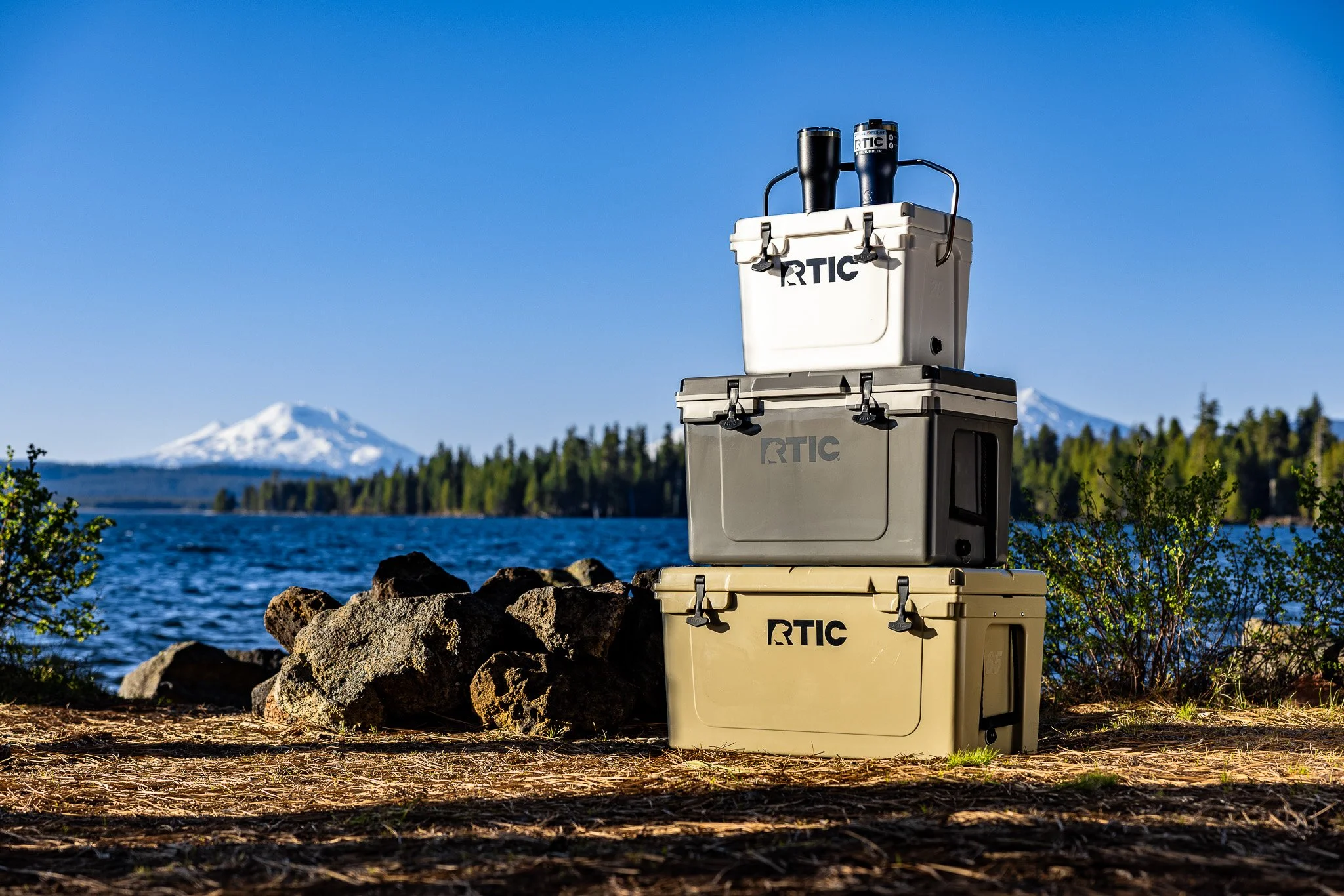 Three stacked storage containers labeled RTVIC near a lake with snow-capped mountains in the background.