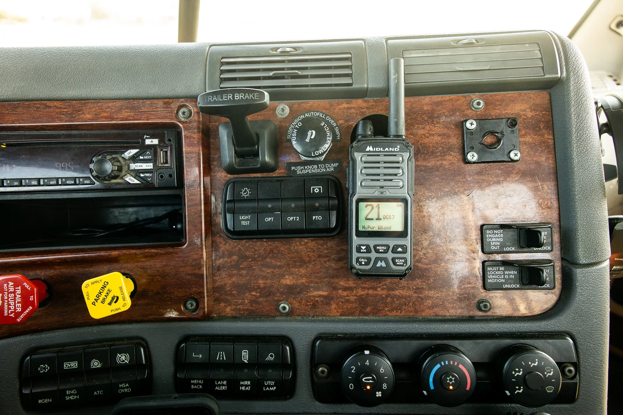 Dashboard of a vehicle with a wood grain finish, displaying various controls, gauges, a radio, a radio communication device, and switches.