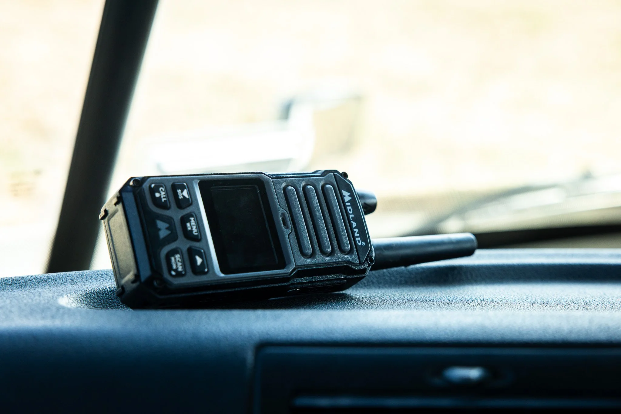 A black Midland two-way radio placed on a vehicle dashboard, with a blurred windshield in the background.