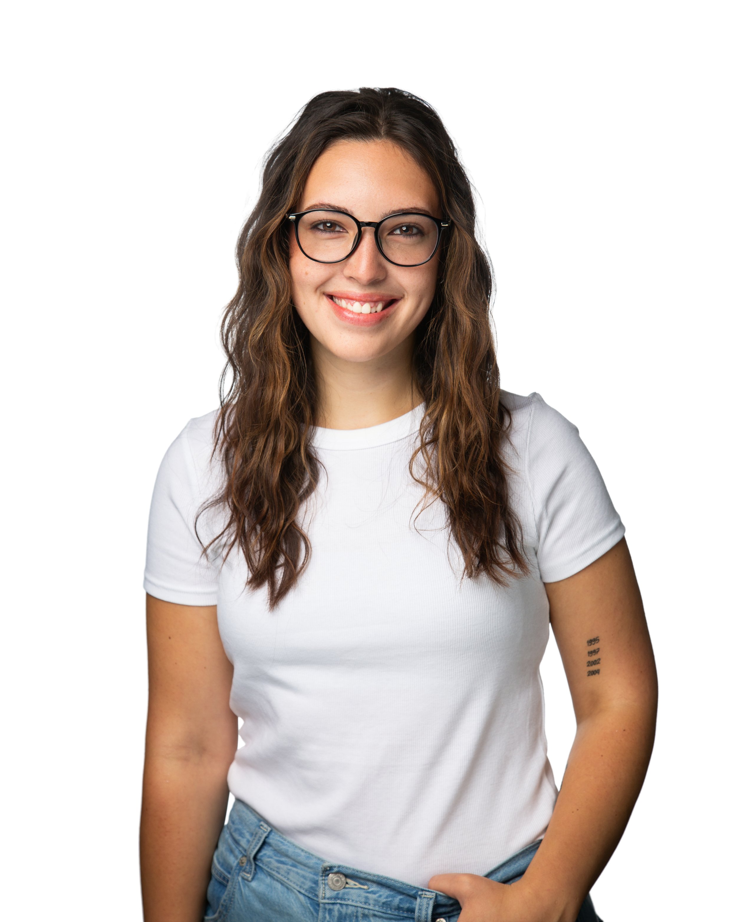 A woman with wavy brown hair, wearing glasses and a white t-shirt, smiling against a white background.