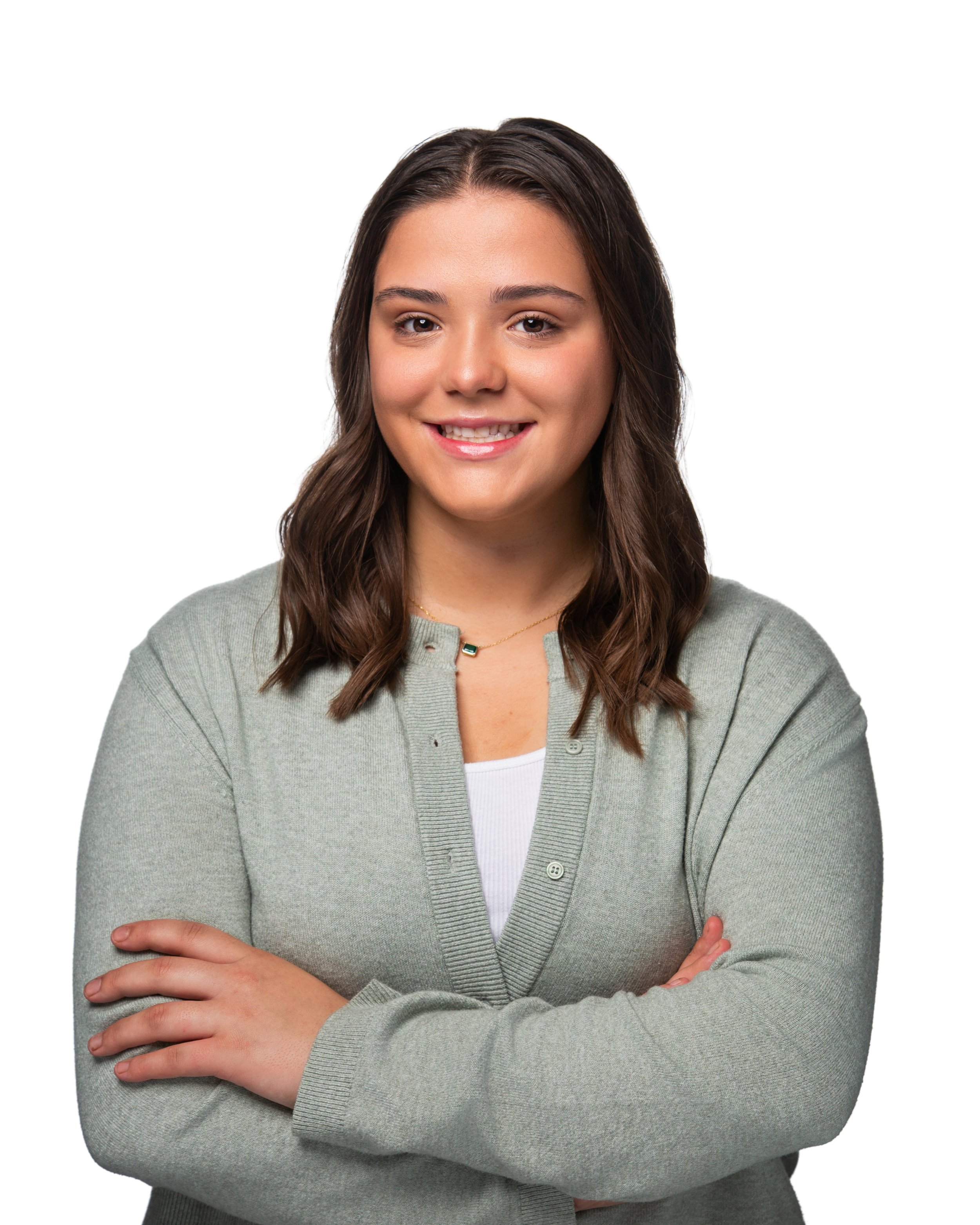 Young woman with long wavy brown hair, smiling, wearing a light gray cardigan over a white top, crossed arms, standing against a white background.