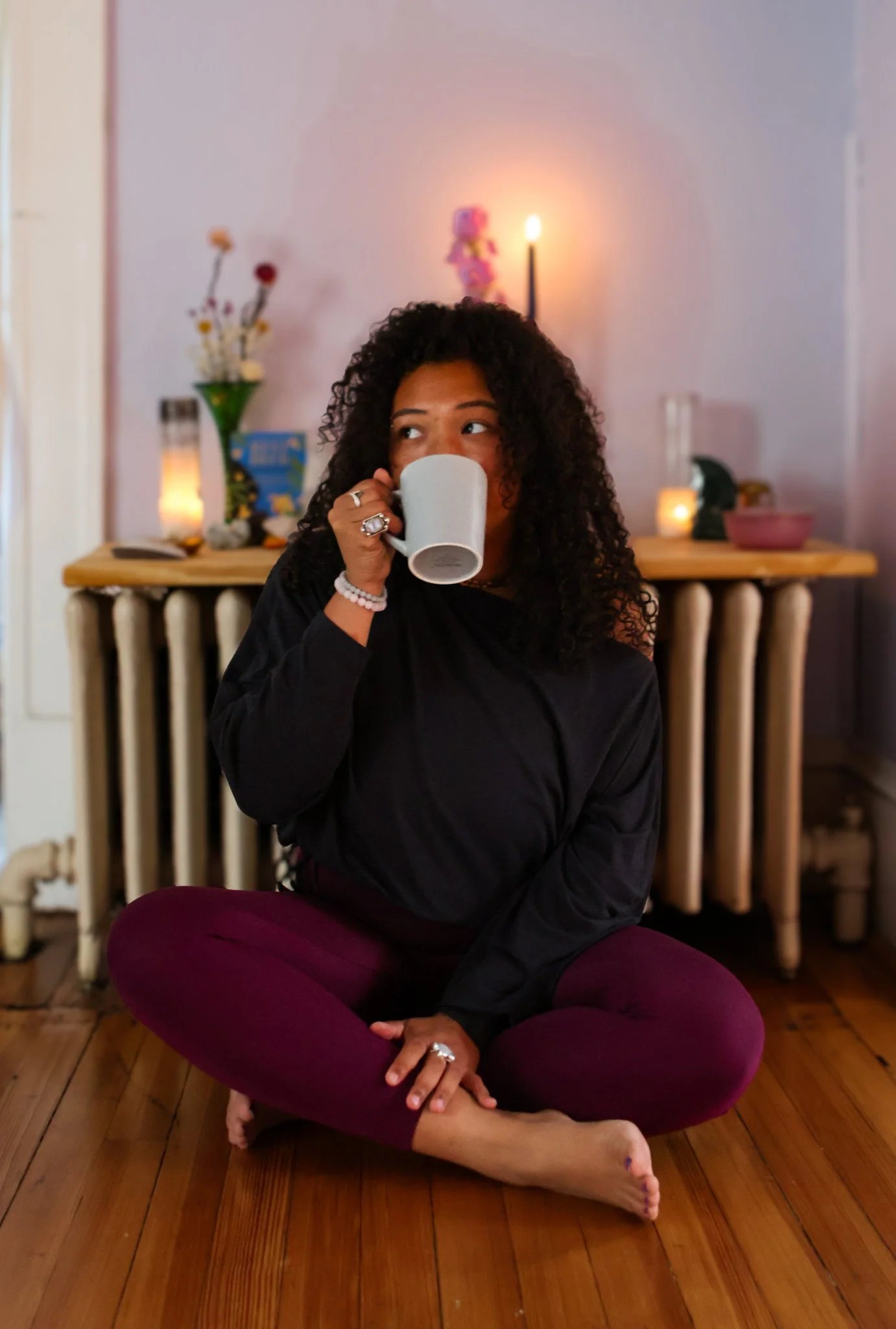 woman with curly hair and brown skin,  sitting cross-legged on the floor, sipping from a mug