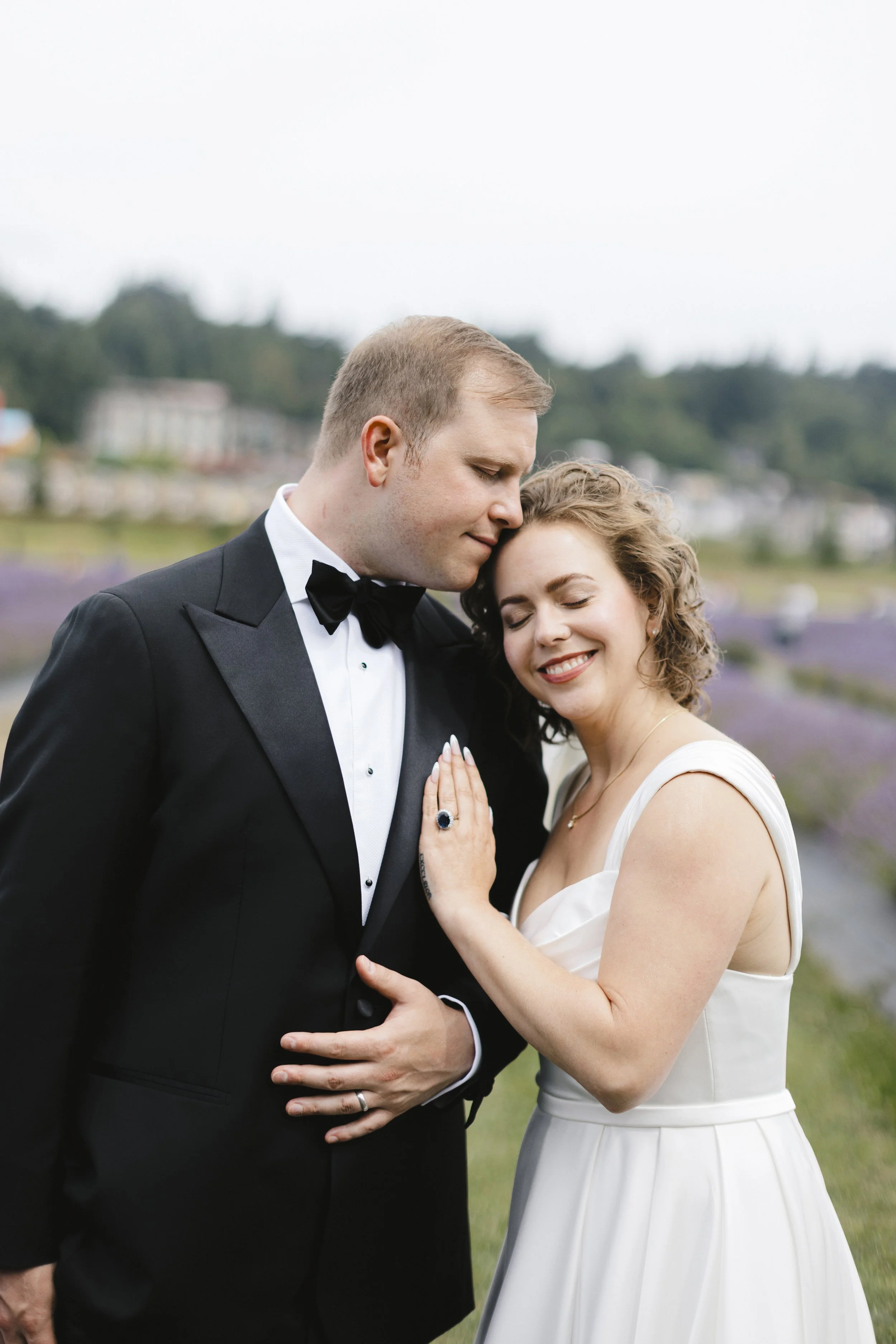 A couple dressed in wedding attire sharing an intimate moment outdoors, with lavender fields in the background.