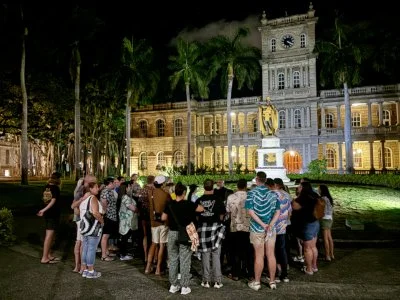 Honolulu ghost tour crowd listens to ghost stories at night in front of the Kamehameha Statue on the Ghosts of Old Honolulu tour