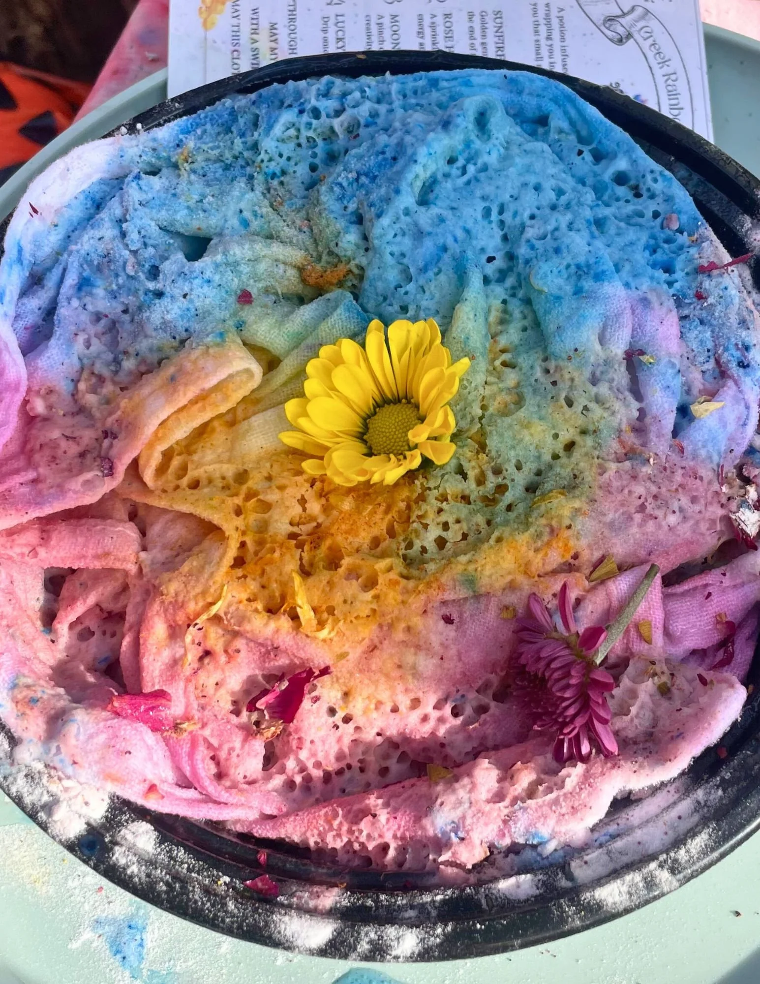 Colorful, melted soap with flowers on top in a round black container.