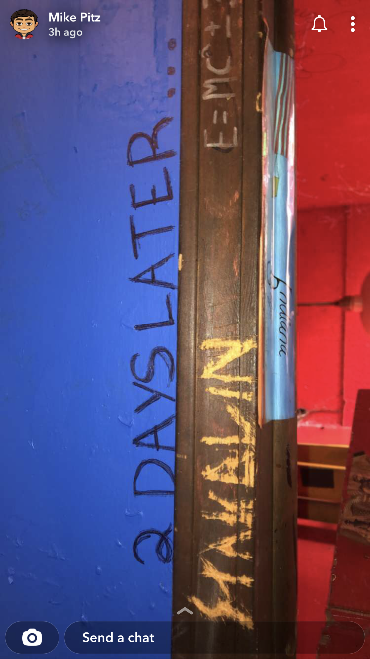 A wooden plank with the message 'DASLATER' written in large black letters, with some additional writing and paint on it, with a red background and a blue wall in the background.