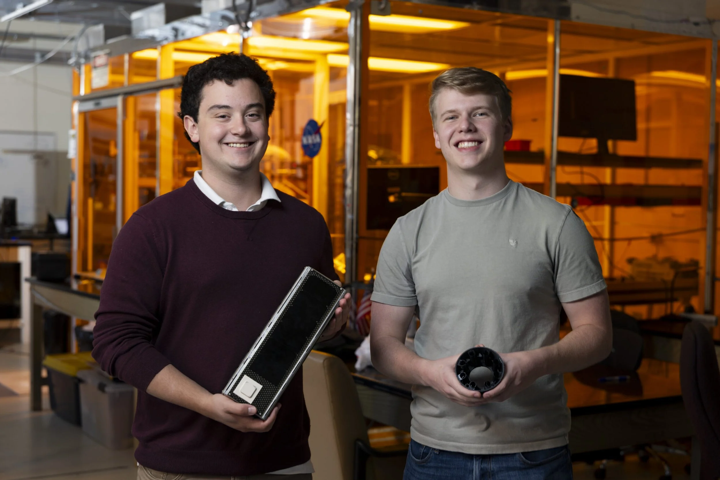 Two UGA students holding a shoe box-sized satellite in a laboratory.