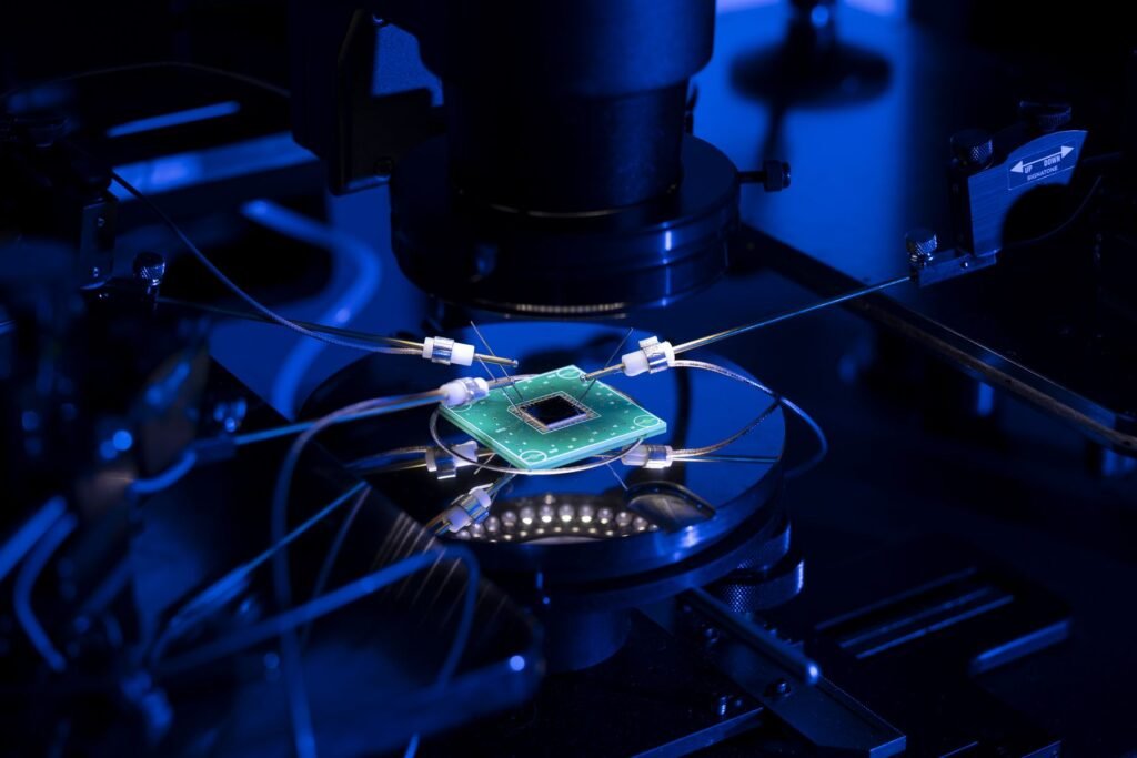 A large computer chip sits on a display that looks like a small turntable. The chip is poked and prodded by small metal rods. The chip is lit up but the rest of the photo is washed in a dark blue light.