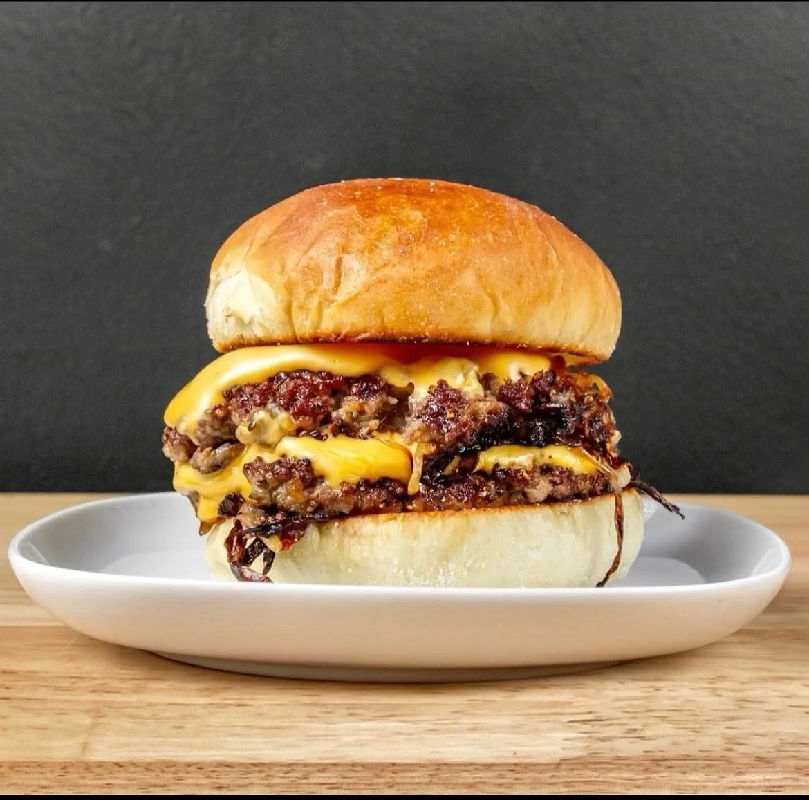 Double cheeseburger with beef patties, melted cheese, and a bun on a white plate.