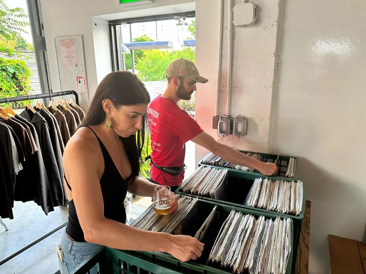 Two people browsing through vinyl records in a store, with clothing items on hangers nearby.
