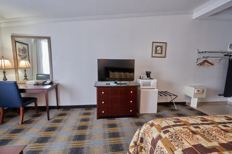 Hotel room interior with a bed, flat-screen TV on a dresser, small refrigerator, microwave, desk with chair, and clothes hangers.
