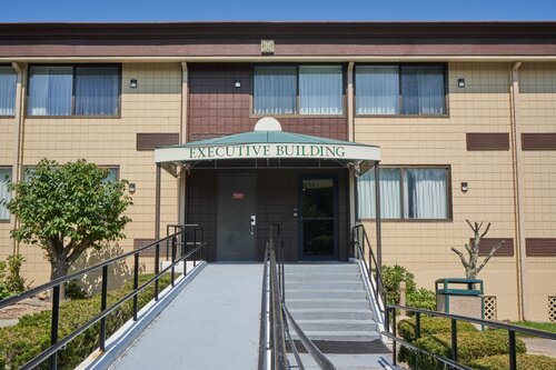 Front entrance of a two-story executive building with an accessible ramp and greenery.