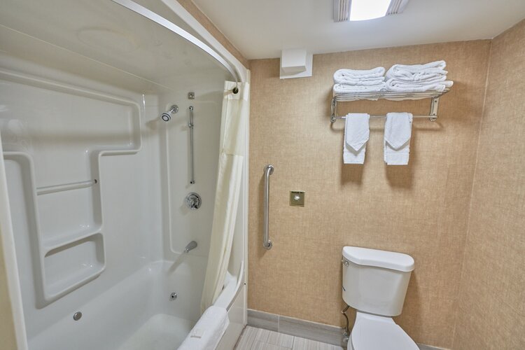 Hotel bathroom with a bathtub-shower combo, shower curtain, grab bars, toilet, and towel rack with folded towels.