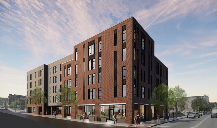 Modern multi-story brick building with retail shops on the ground level, pedestrians walking on the sidewalk, trees, and parked cars in an urban setting during sunset.