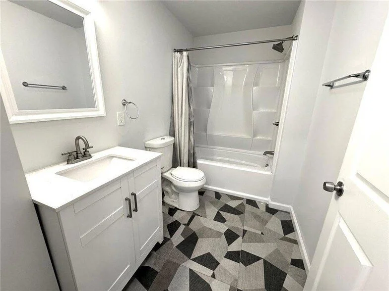A small bathroom with a white vanity, a mirror, a toilet, and a bathtub with a shower.