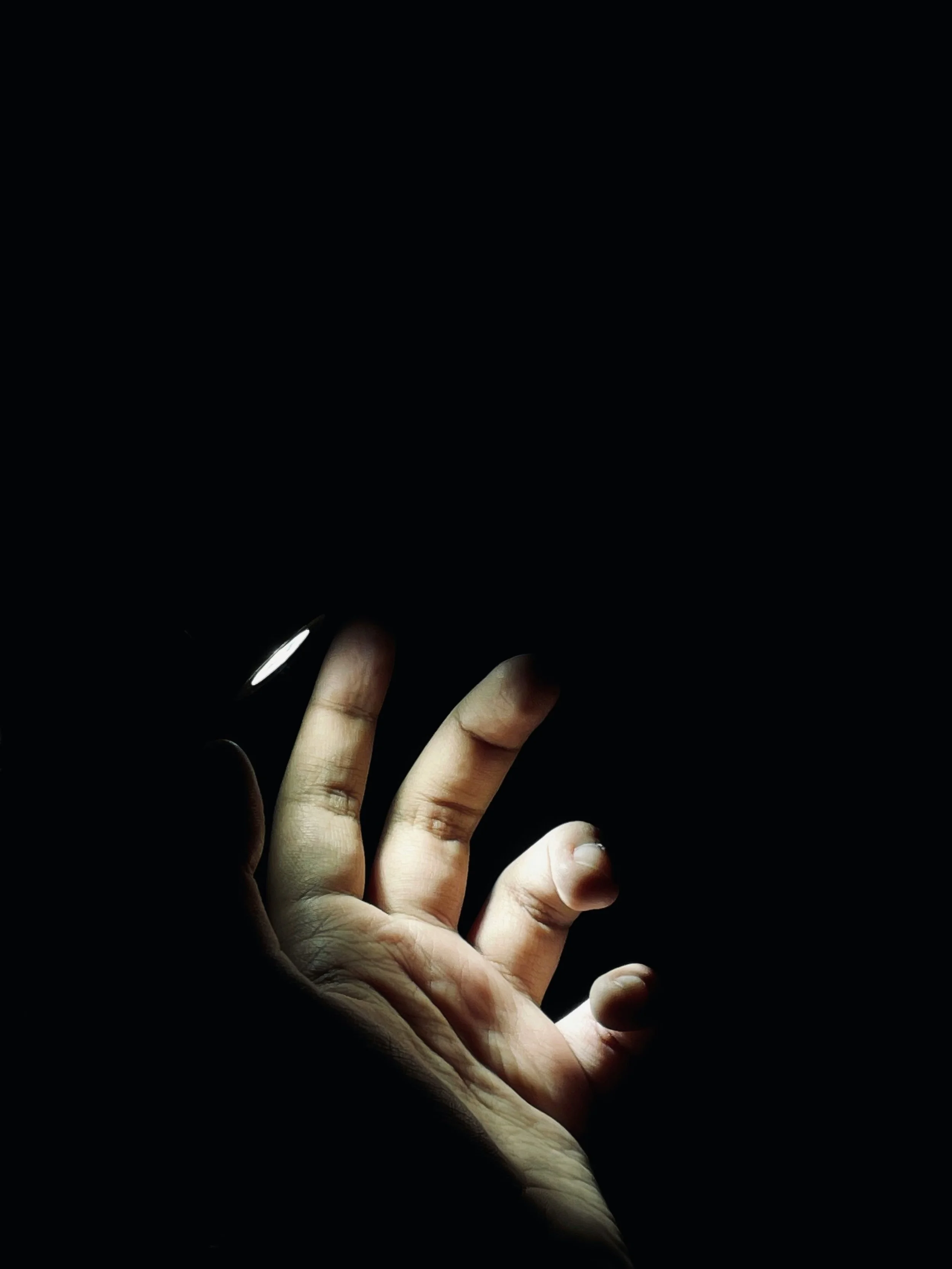 A hand is illuminated in a dark environment, with only the fingers visible against the black background.