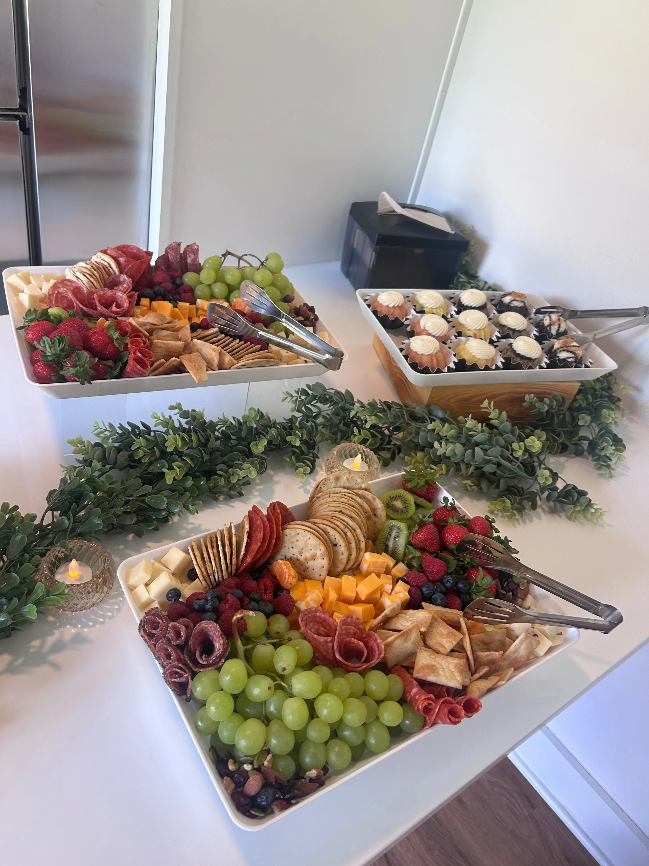 Overhead view of a brunch table with various dishes, including waffles topped with fruit and syrup, vegetable frittata, salads, granola with berries, and glasses of orange juice, coffee, and tea, set on a light blue tablecloth with white chairs and a vase with yellow flowers.