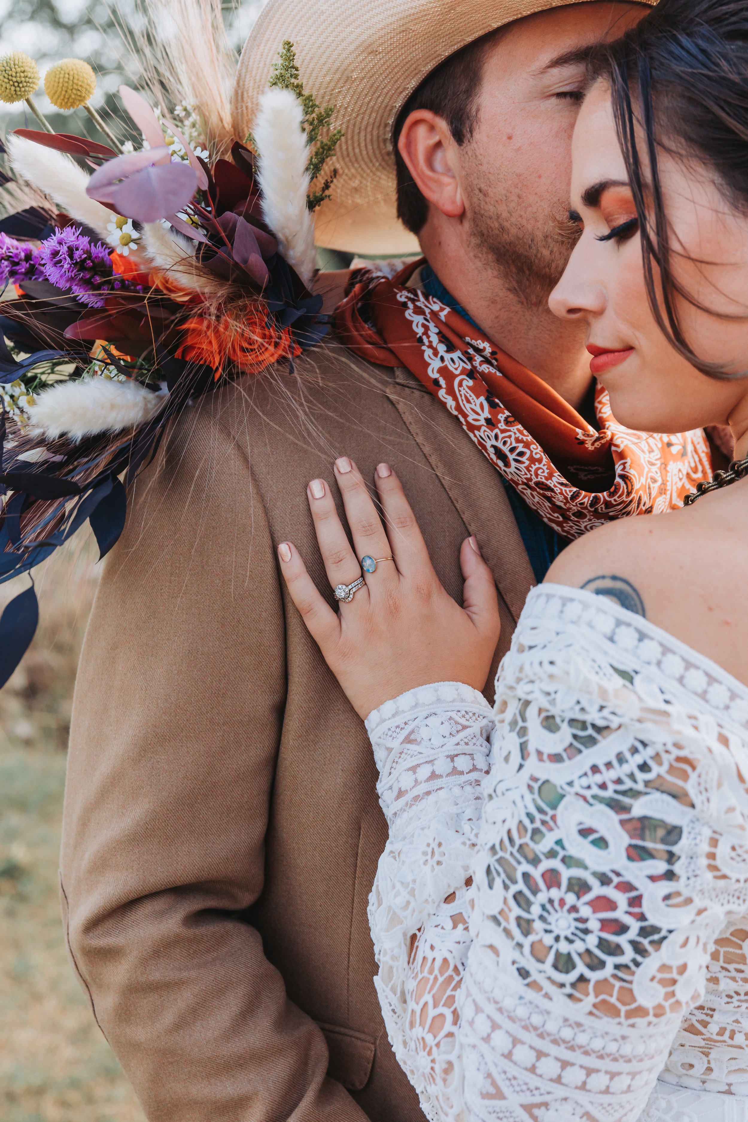 Close-up of a bride resting her hand on her groom's shoulder, highlighting her engagement ring and crochet wedding sleeve during a western-inspired outdoor wedding.