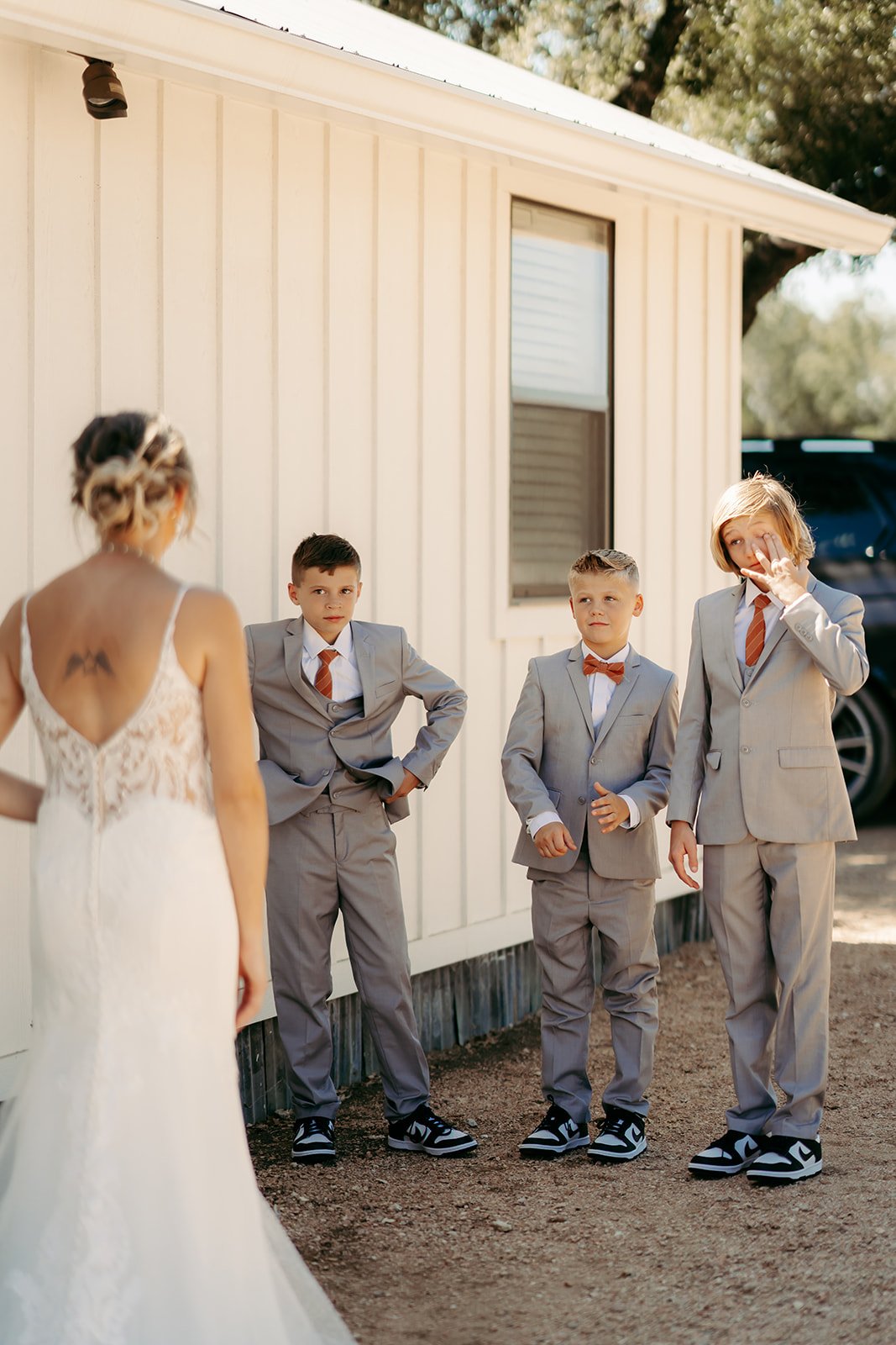 Three young boys in gray suits react emotionally as they see the bride for the first time during a wedding first look moment.