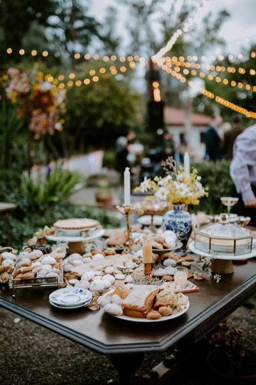 Outdoor wedding dessert table styled with assorted pastries, stone accents, and candlelight for an elegant garden reception.