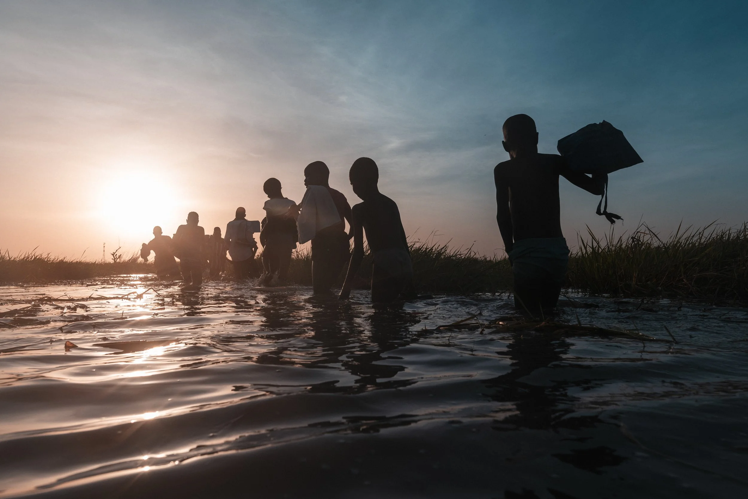 At sunrise, pupils wade through the Sudd wetlands on their way to school. The daily route crosses waist-deep water where snakes and crocodiles are a risk.