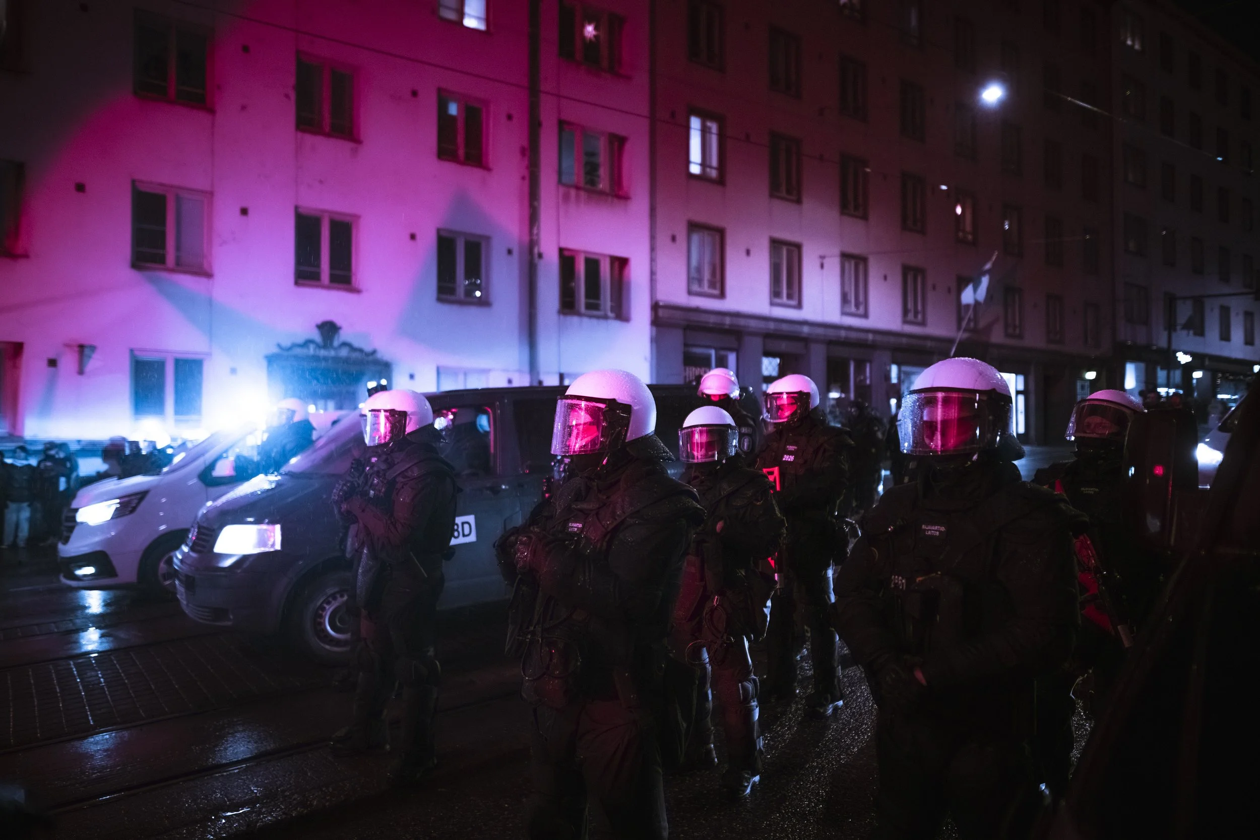 Police officers and border guards in riot gear hold a cordon on a rain-slick street in Töölö, Helsinki, separating the Helsinki Without Nazis counter-demonstration from the 612 torch march on Finland’s Independence Day.