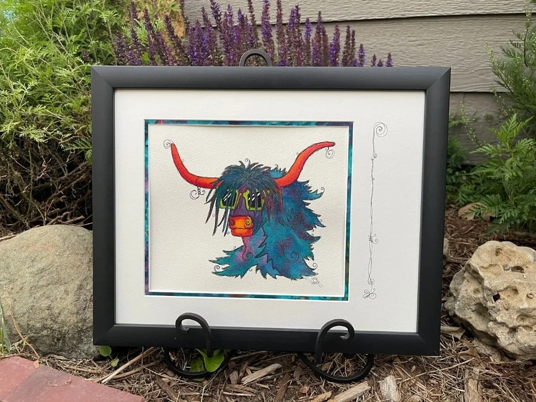 Angus McFloof’nHoof, a colorful watercolor Highland cow in lime sunglasses, surrounded by a hand-painted mat in deep blues, teals, and purples and finished in a matte-black frame.