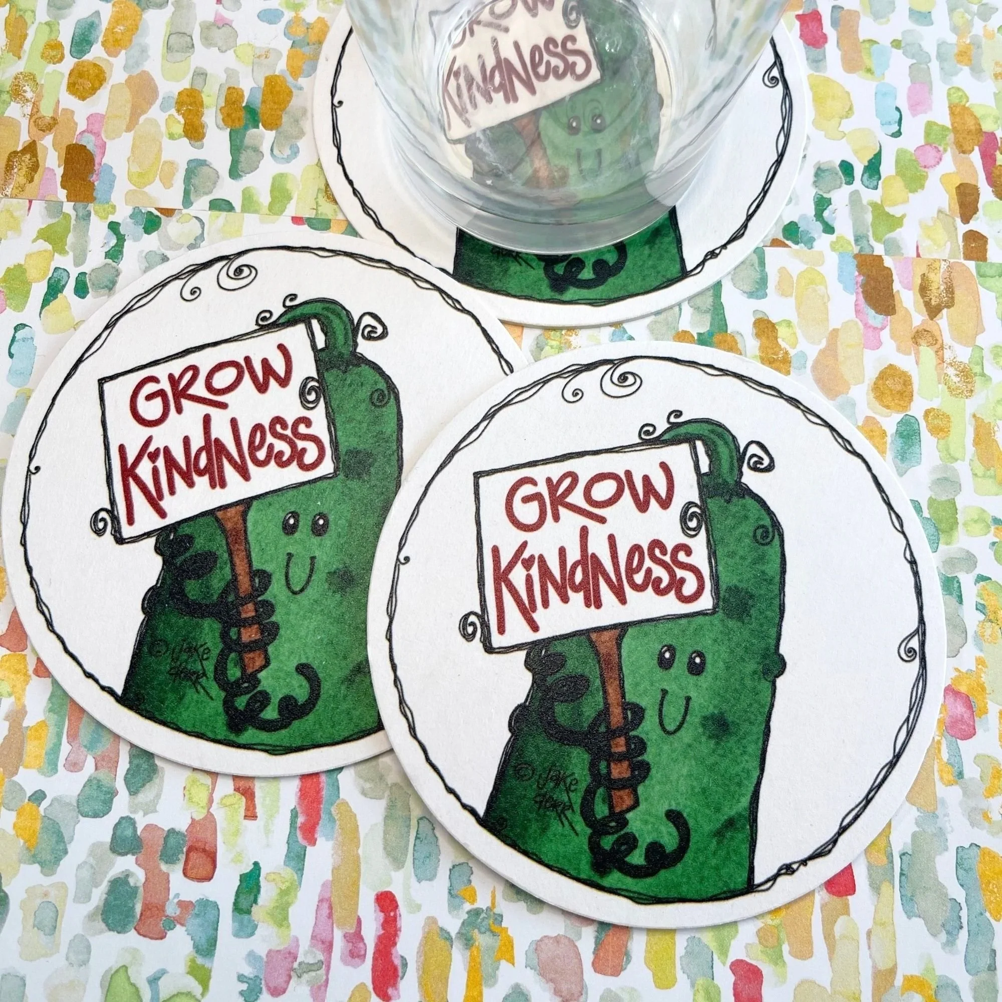 three cucumber kindness crew drink coasters on tabletop with clear glass resting on one showing real use