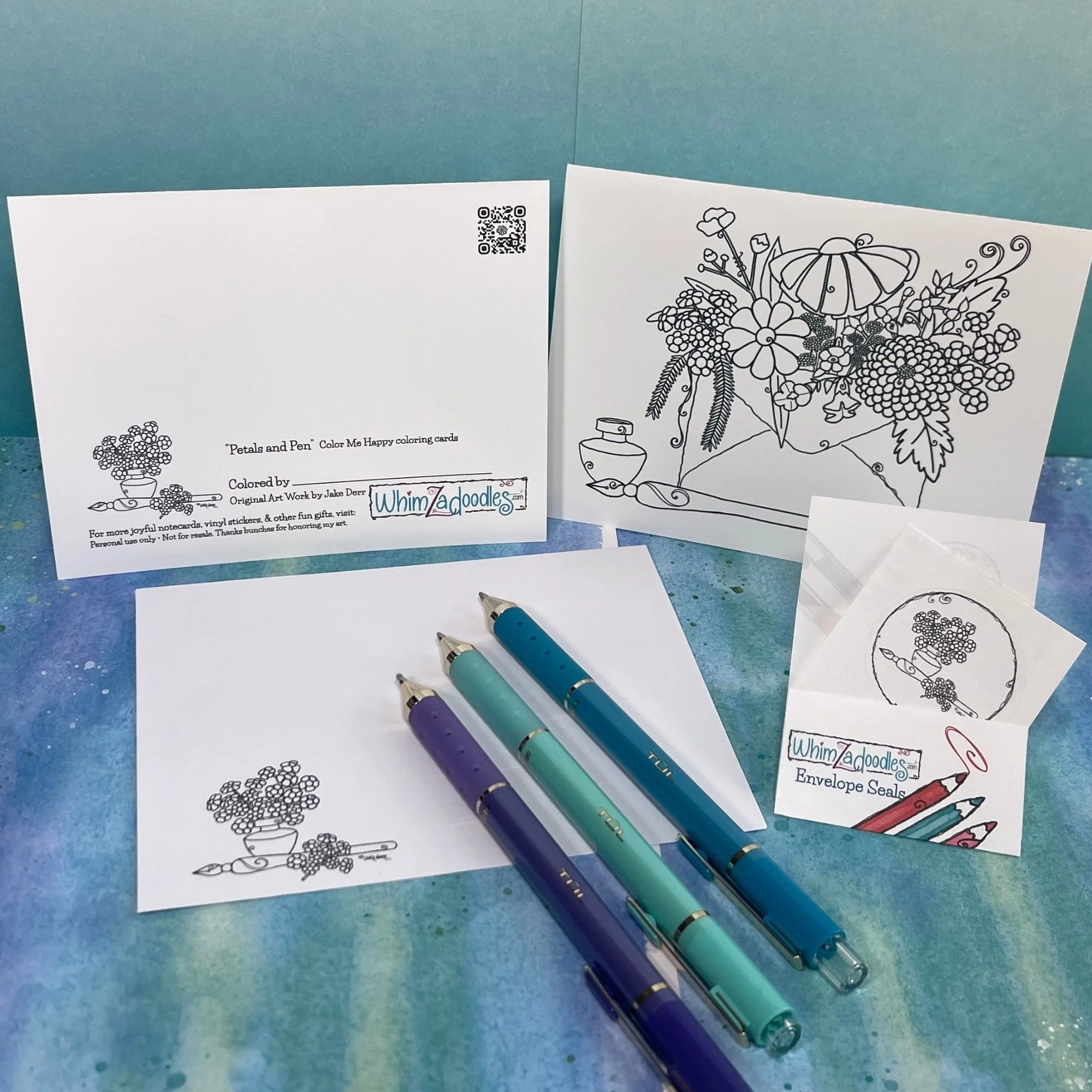 coloring card set with envelope, seal, and gel pens arranged on teal background ready for decorating