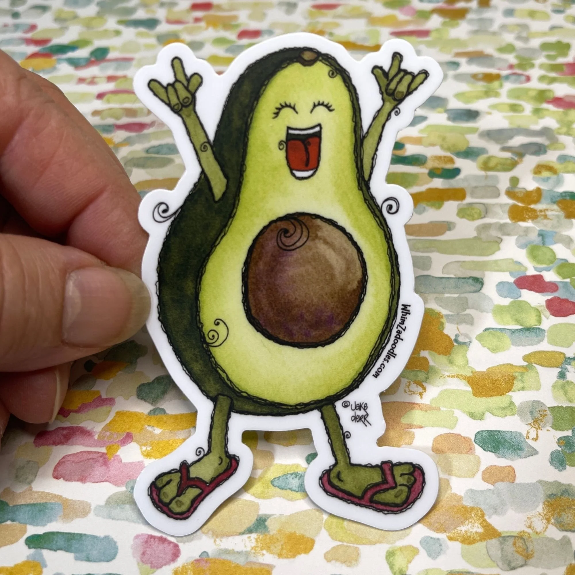 Hand holding avocado sticker to show size and detail of smiling “I love you” design