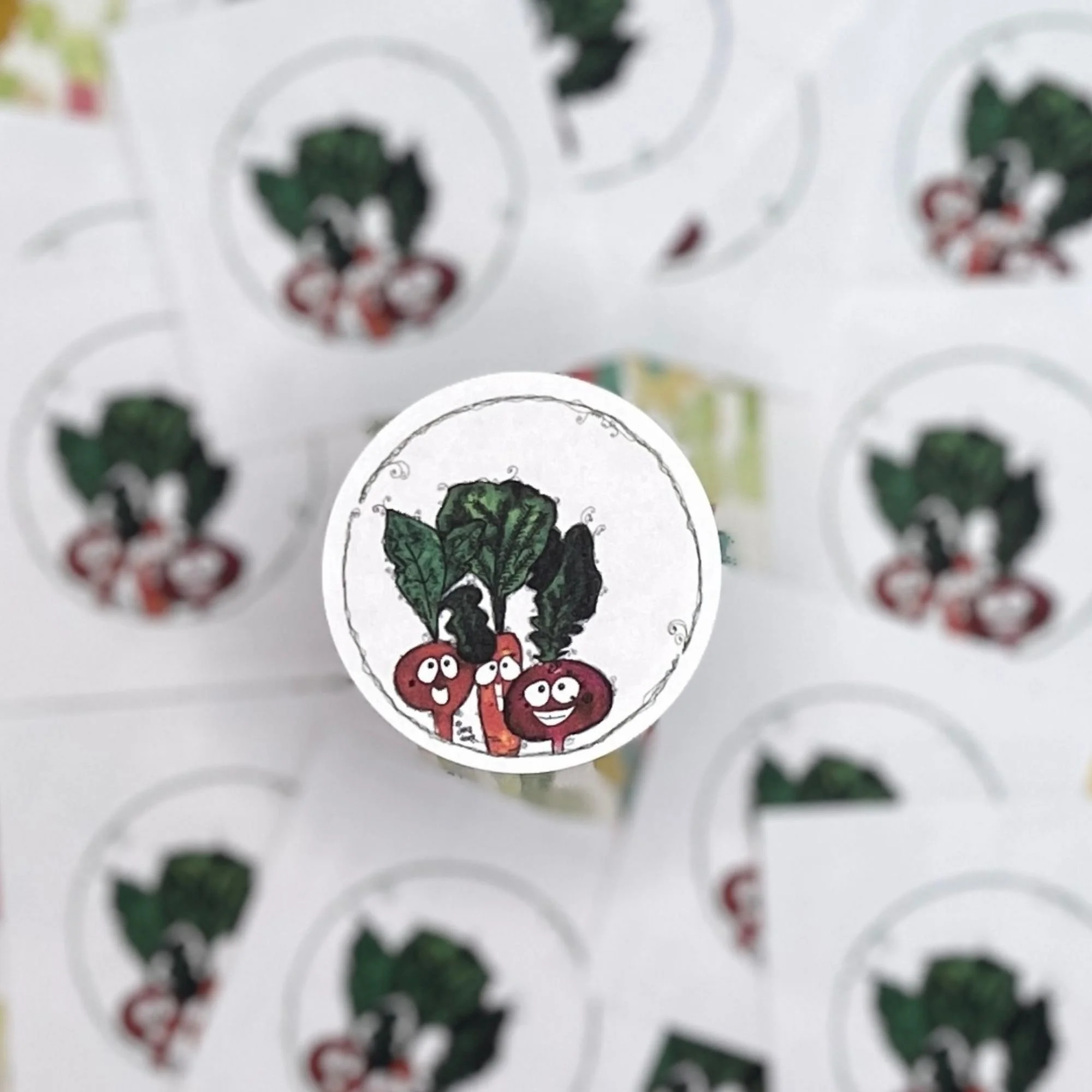close-up of round watercolor vegetable envelope seal with beet carrot and radish characters, scattered seals softly blurred in background