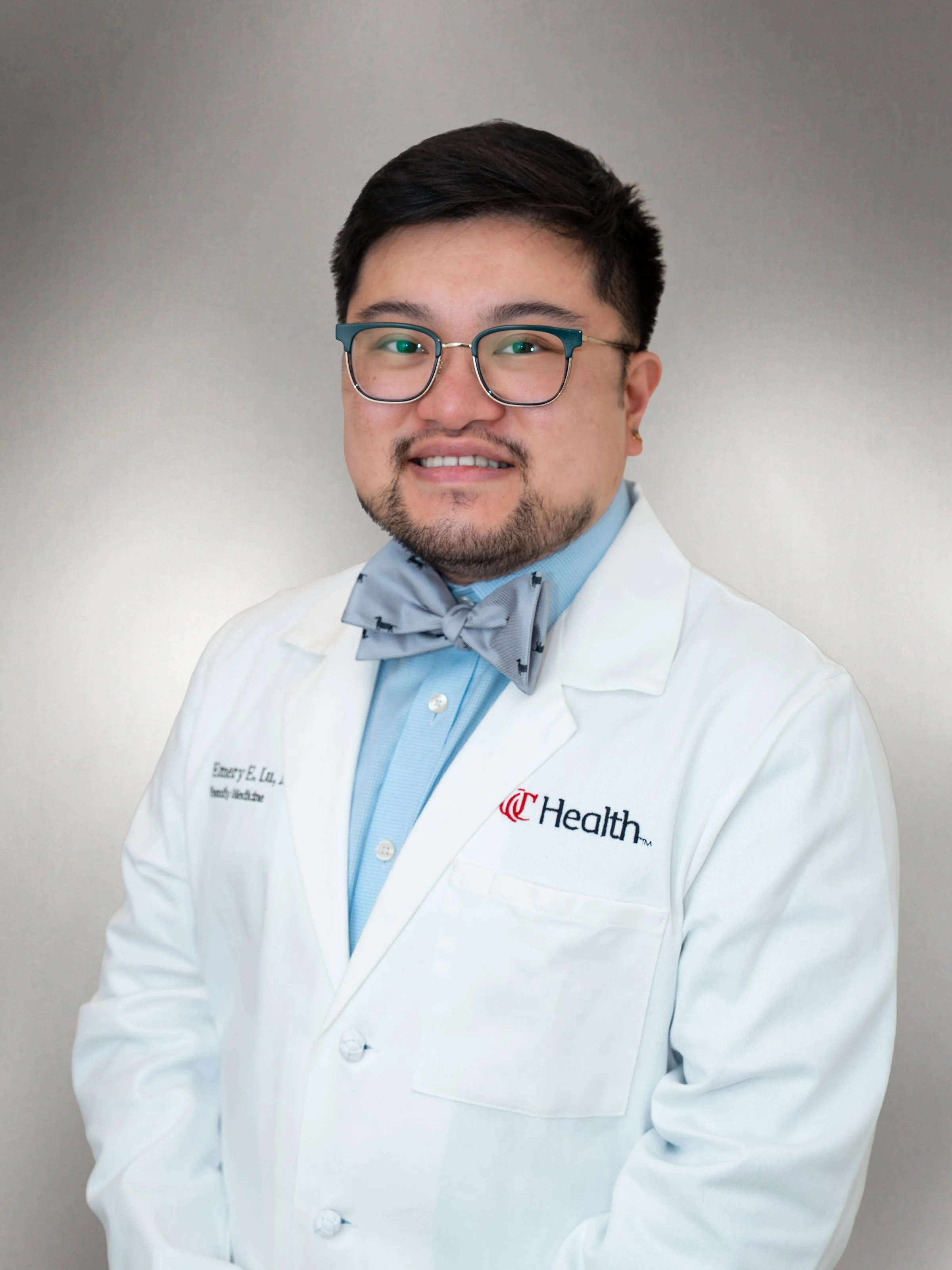 Dr. Emery Lu wearing glasses, a white lab coat, and a gray bow tie in a professional headshot.