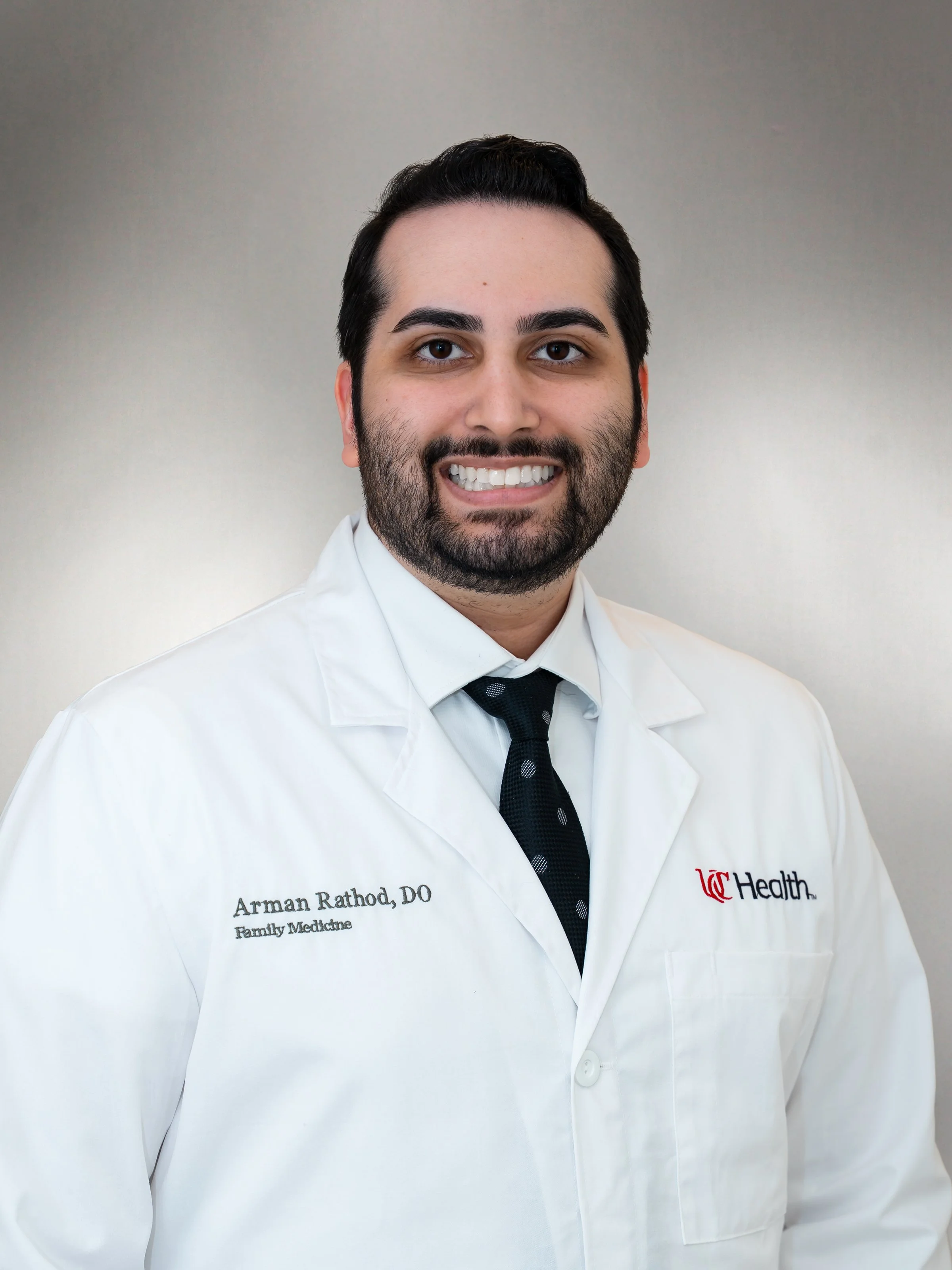Dr. Arman Rathod wearing a white lab coat and dark tie in a professional headshot.