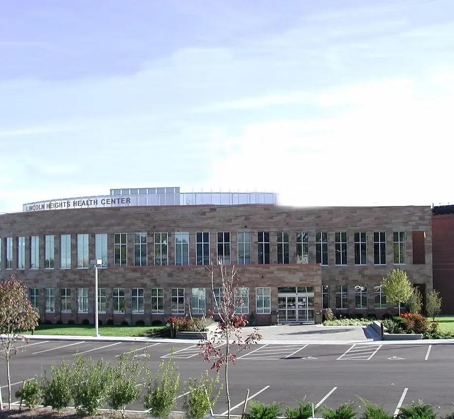 Two-story dark-beige brick building with many rows of windows. On the roof in block letters: LINCOLN HEIGHTS HEALTH CENTER