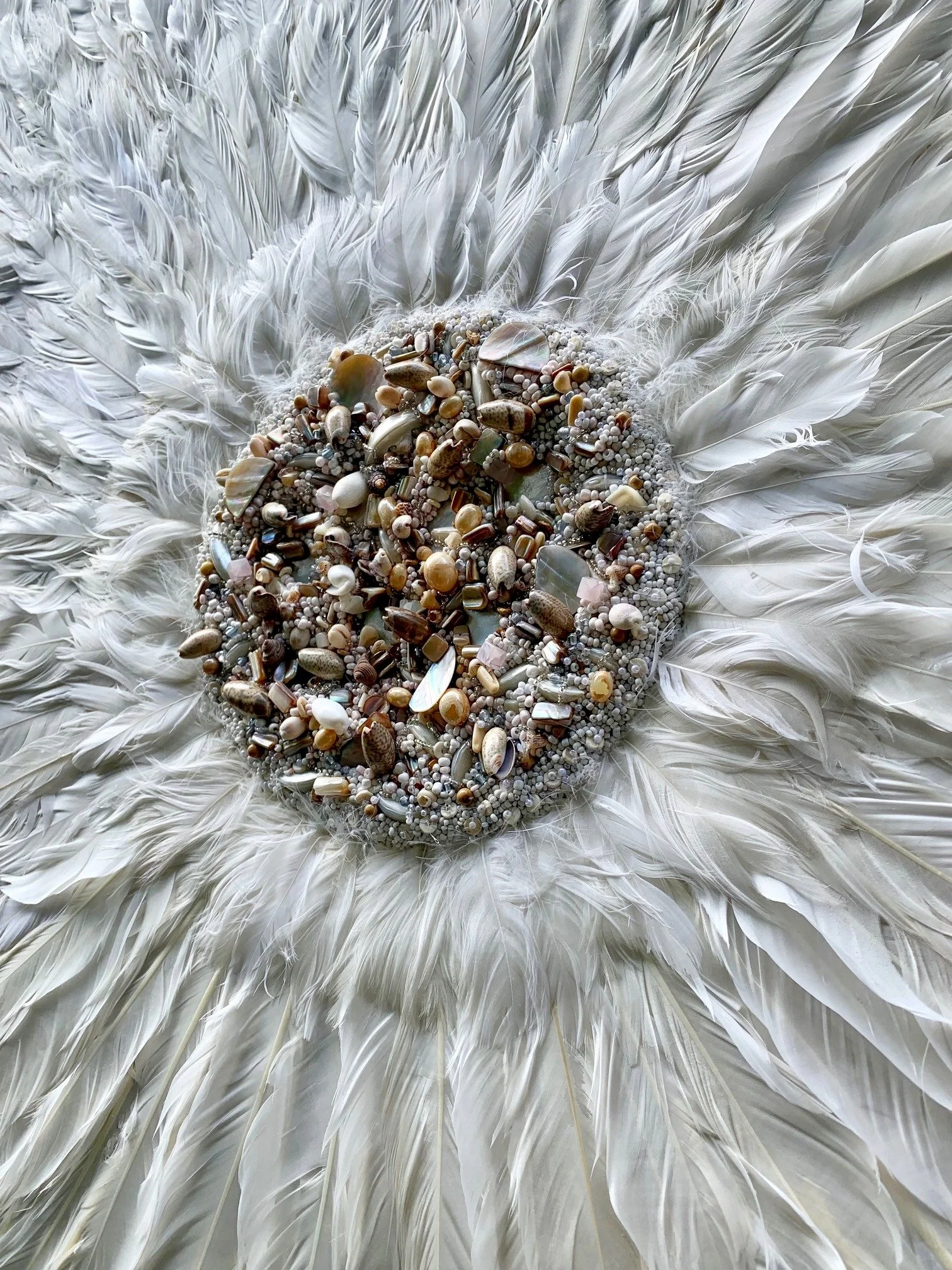 Close-up of a circular arrangement of small shells, beads, and pearls surrounded by white feathers.