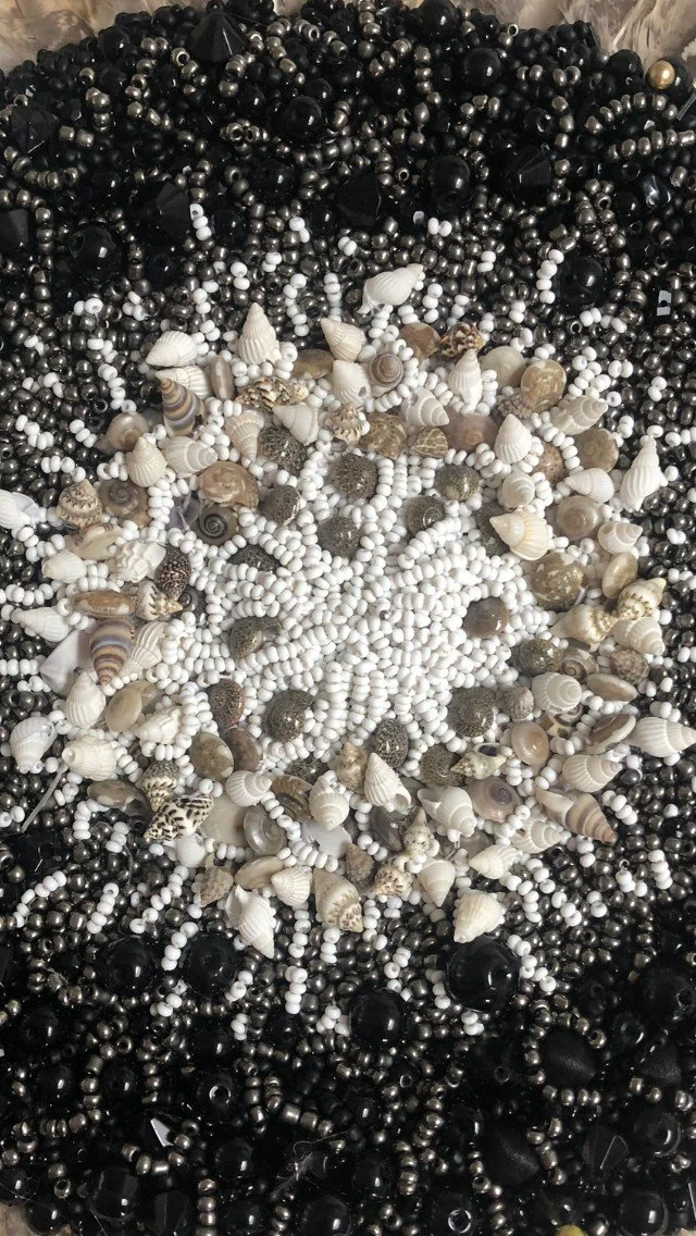 A close-up view of a pile of various seashells and beads in black, white, and gray colors.