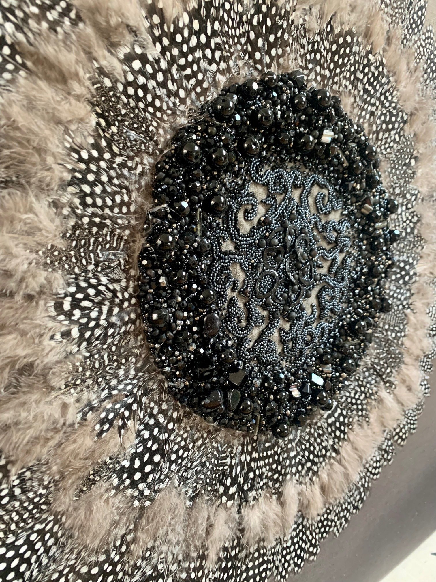 Close-up of decorative feathers and beads in black, silver, and beige colors, arranged in a detailed pattern.