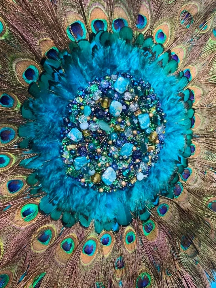 A close-up of a peacock's tail feathers with a collection of blue and green gemstones in the center.