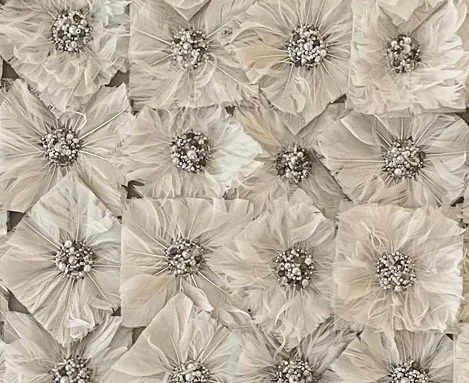 Close-up of a decorative wall made of cream-colored fabric flowers with pearl and rhinestone centers.