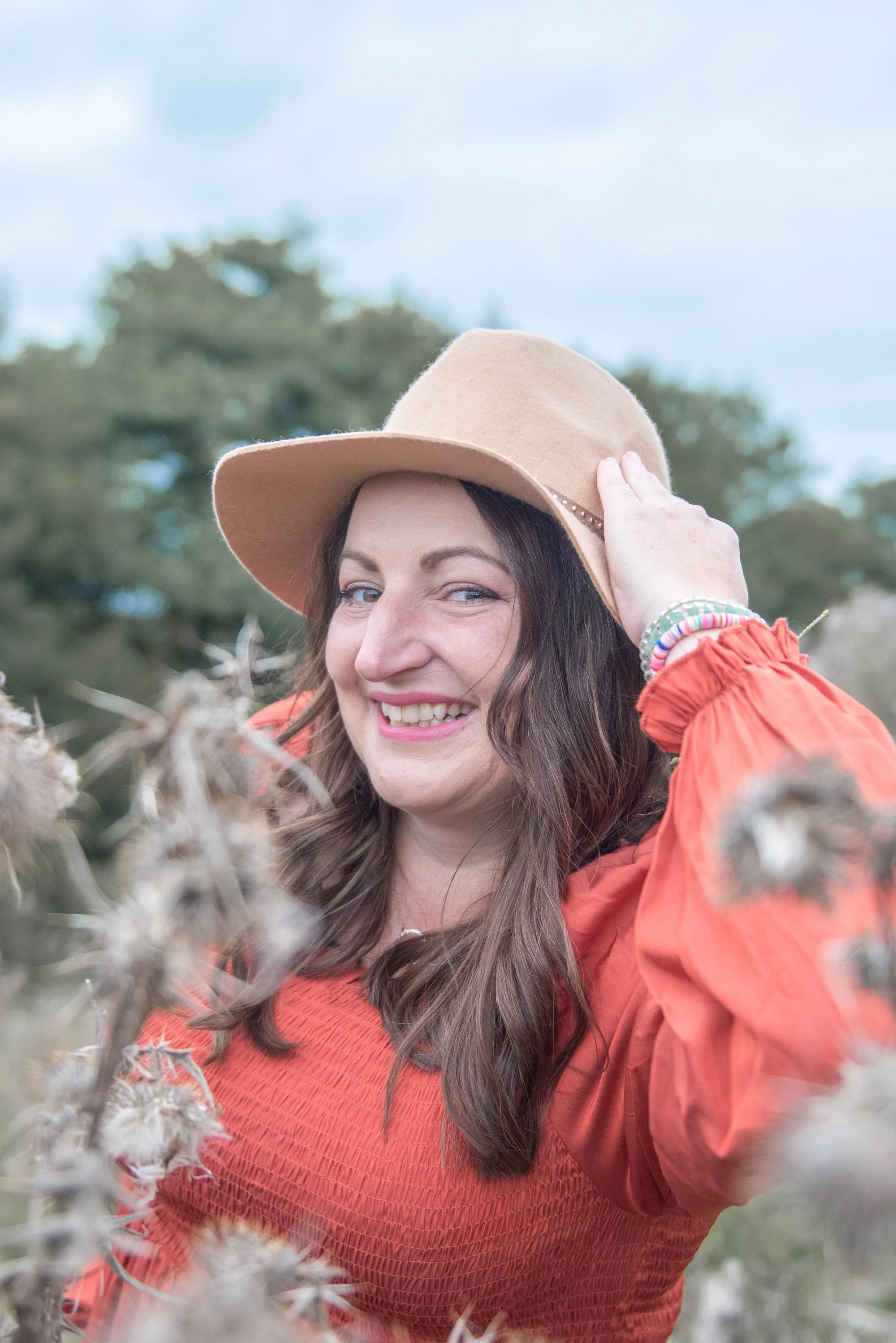 Woman in natural makeup in hat, long brown hair, in nature joyfully smiling to the camera