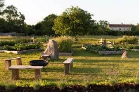 Glastonbury retreat Apothecary Gardens Stone circle with a wooden bench and trees during daytime, with a grassy field and some rocks. In the background, there's a building.