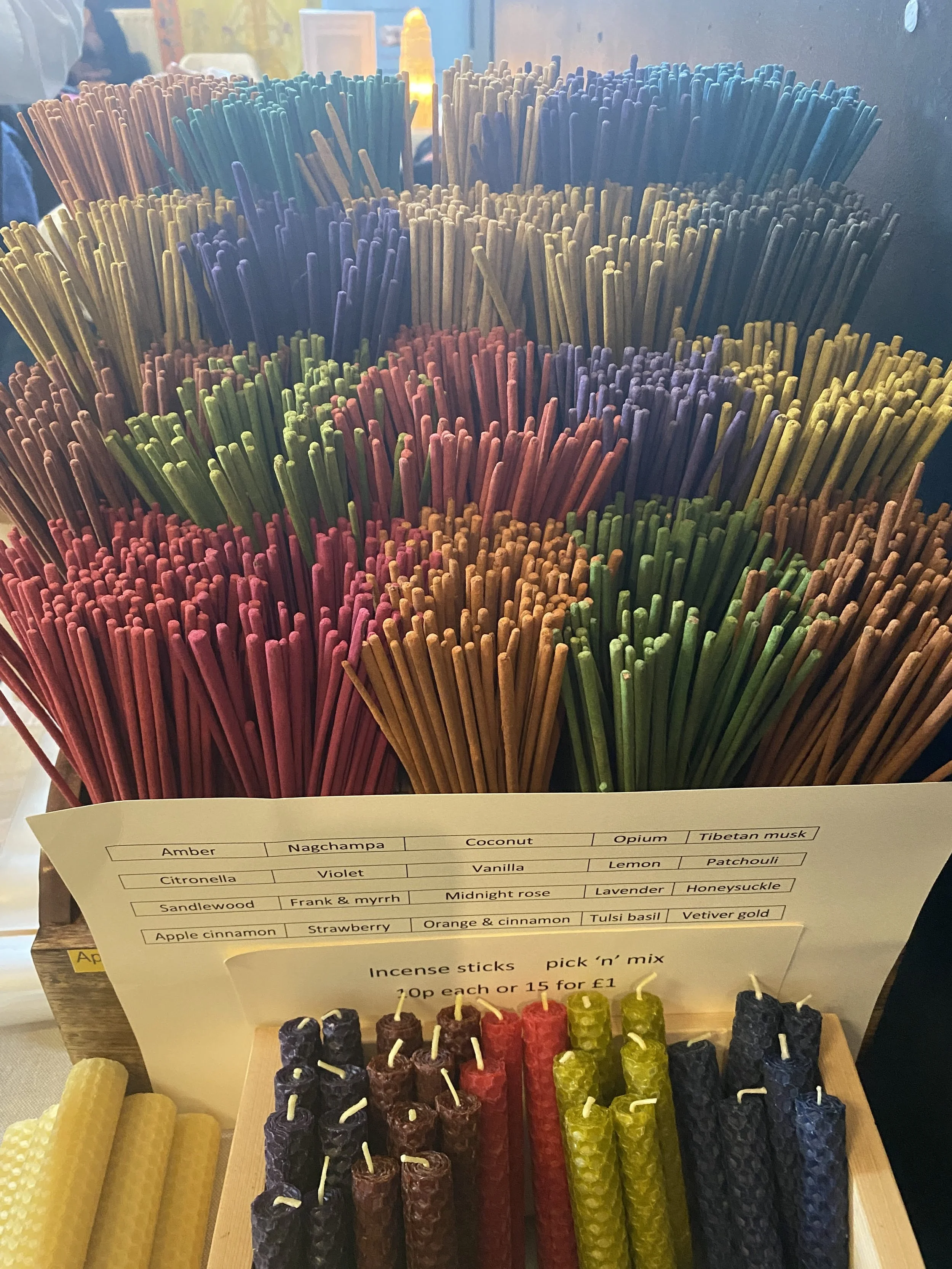 Glastonbury retreat High street. shopping A display of colorful incense sticks arranged vertically with a chart listing different scents, and several beeswax candles in various colors in front.