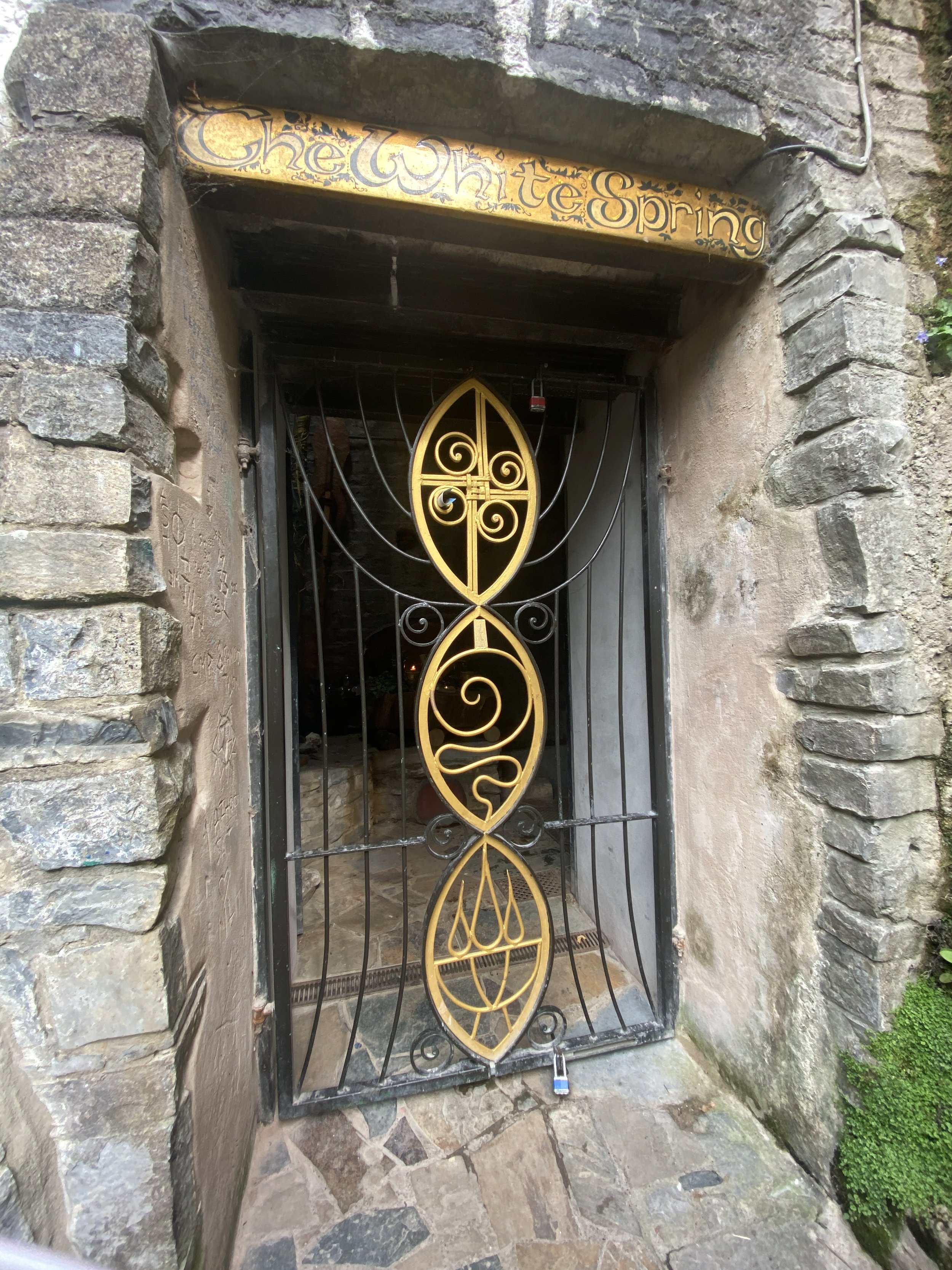 
Glastonbury retreat. White Spring Entrance gate with decorative black and gold wrought iron design and a sign above