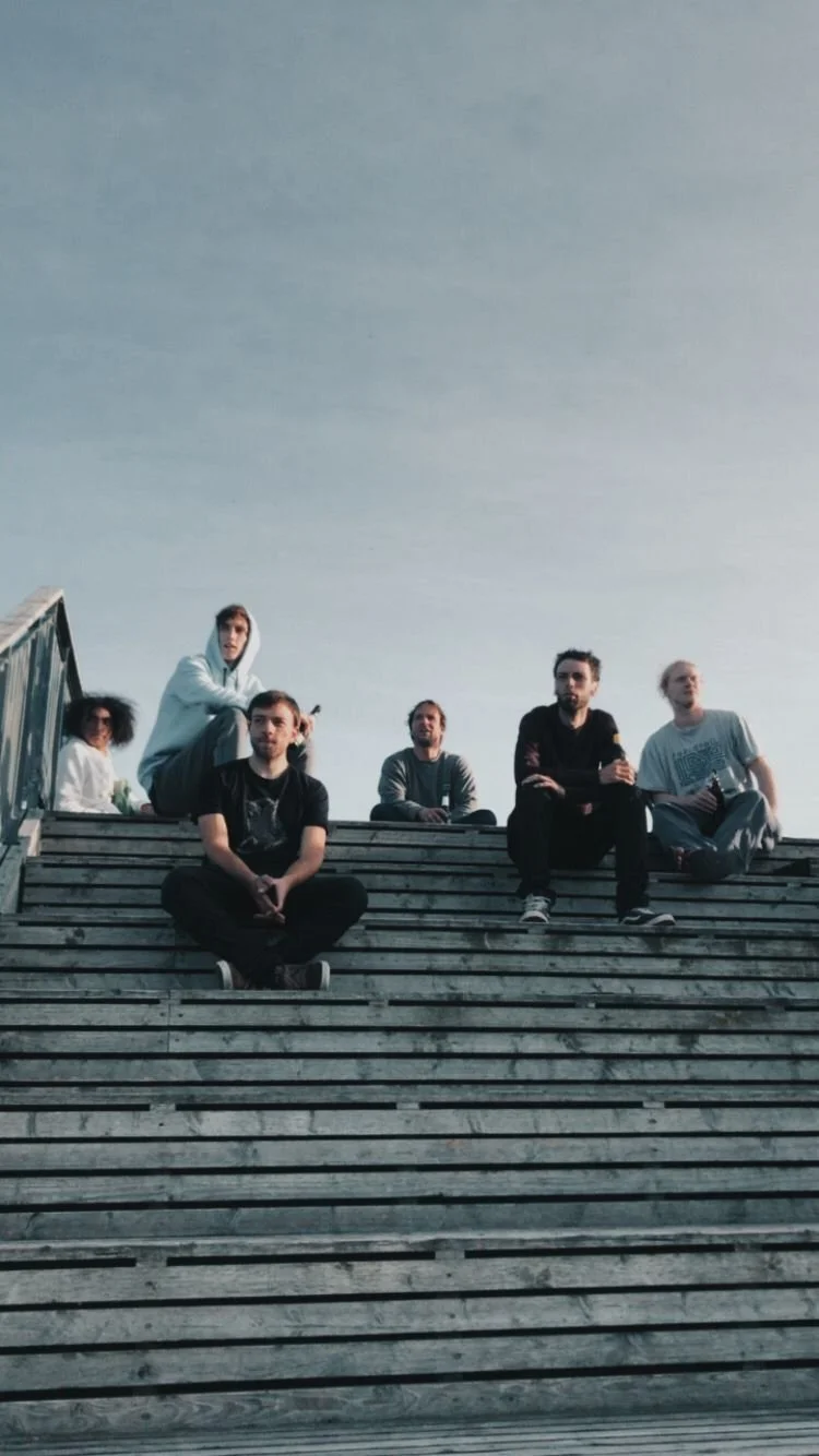 Six people sitting on a wooden staircase outdoors, with a cloudy sky above them.