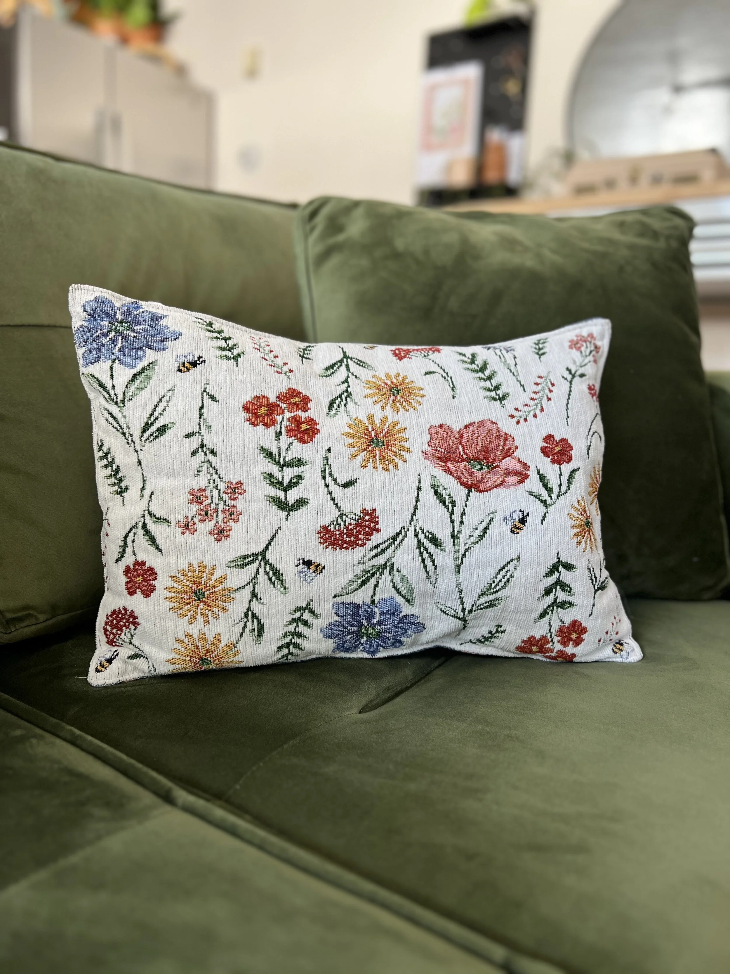 White pillow with embroidered flowers sitting on a green velvet couch